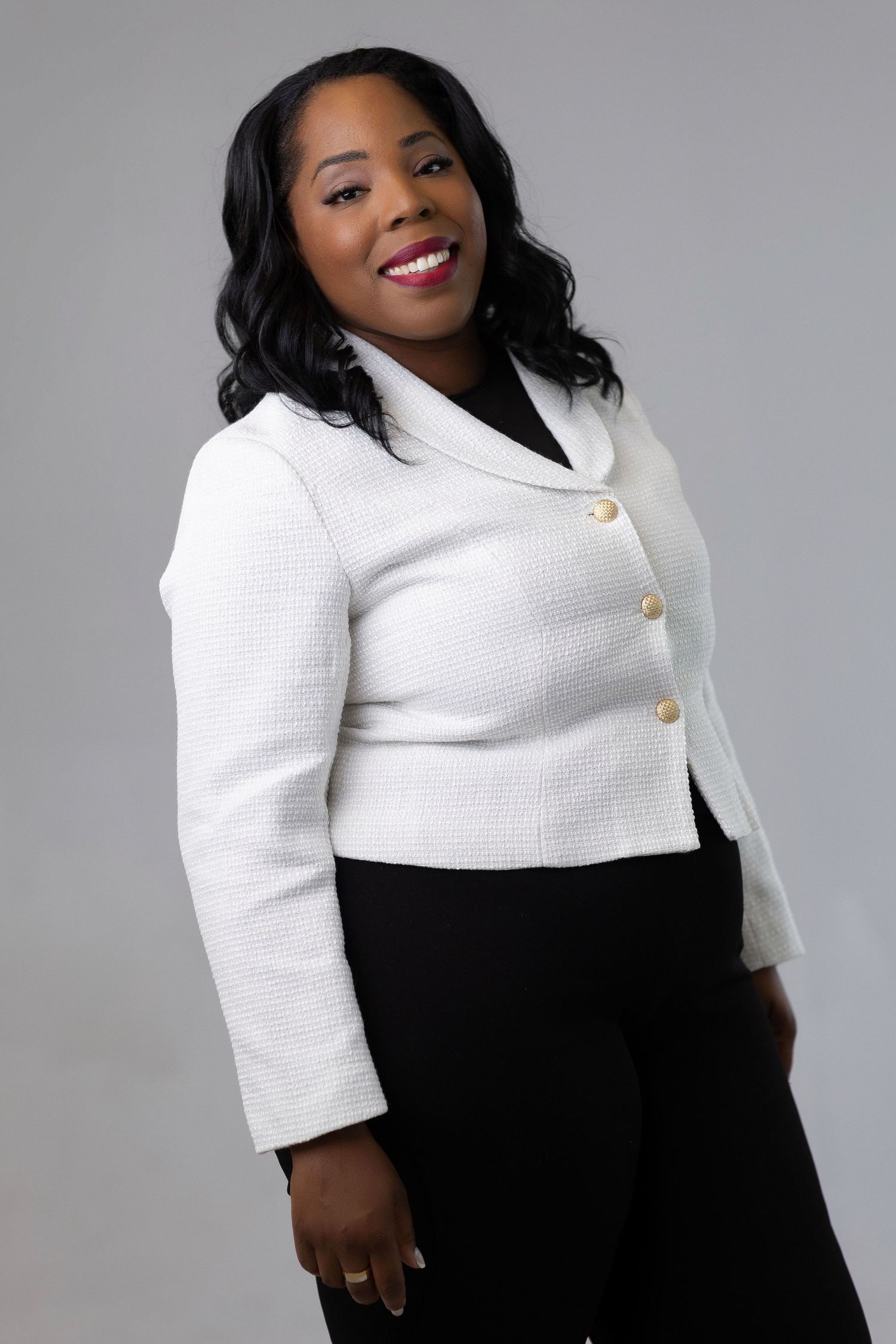 Professional fashion portrait showing a stylish black and white outfit with textured blazer and elegant pose against gray backdrop.