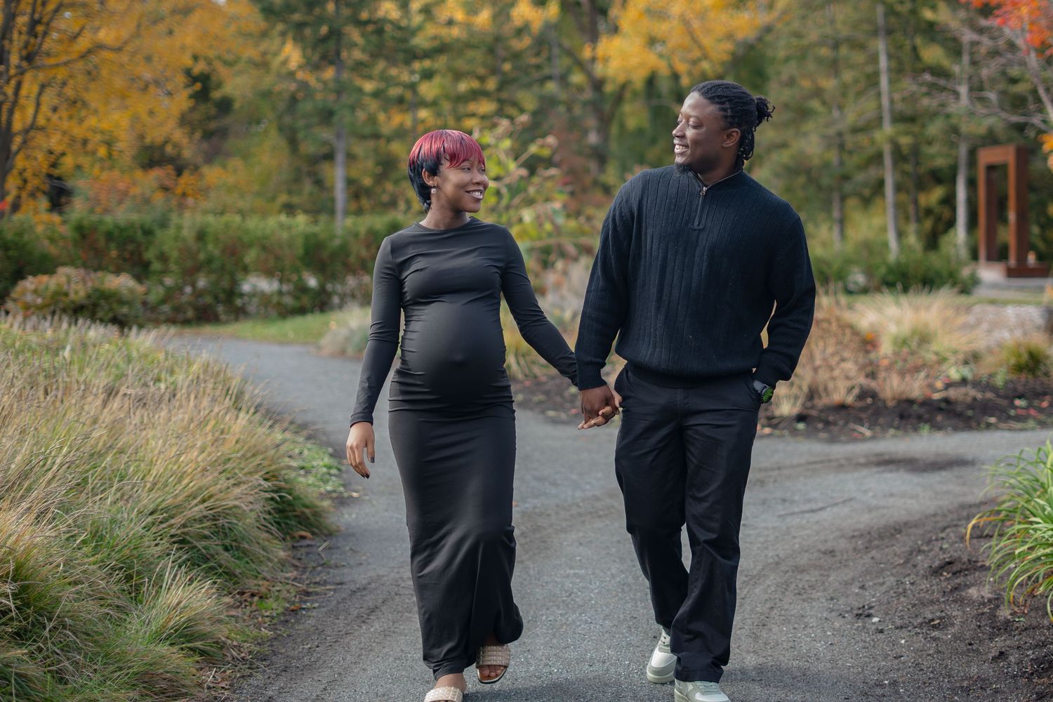 Two people walk together on a winding gravel path through autumn foliage in a park setting.