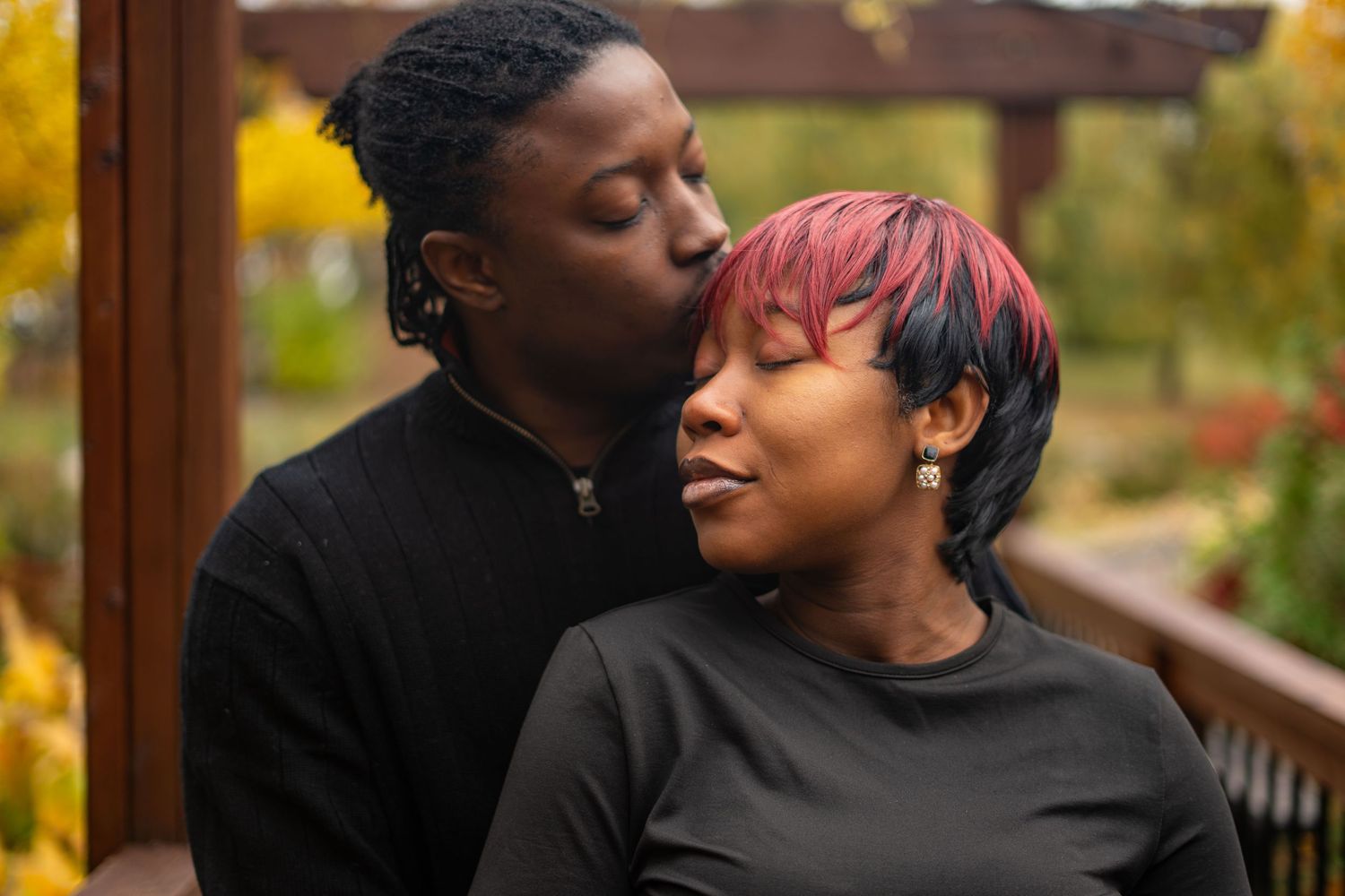 A couple shares an intimate moment together while sitting outdoors on a wooden deck in autumn.