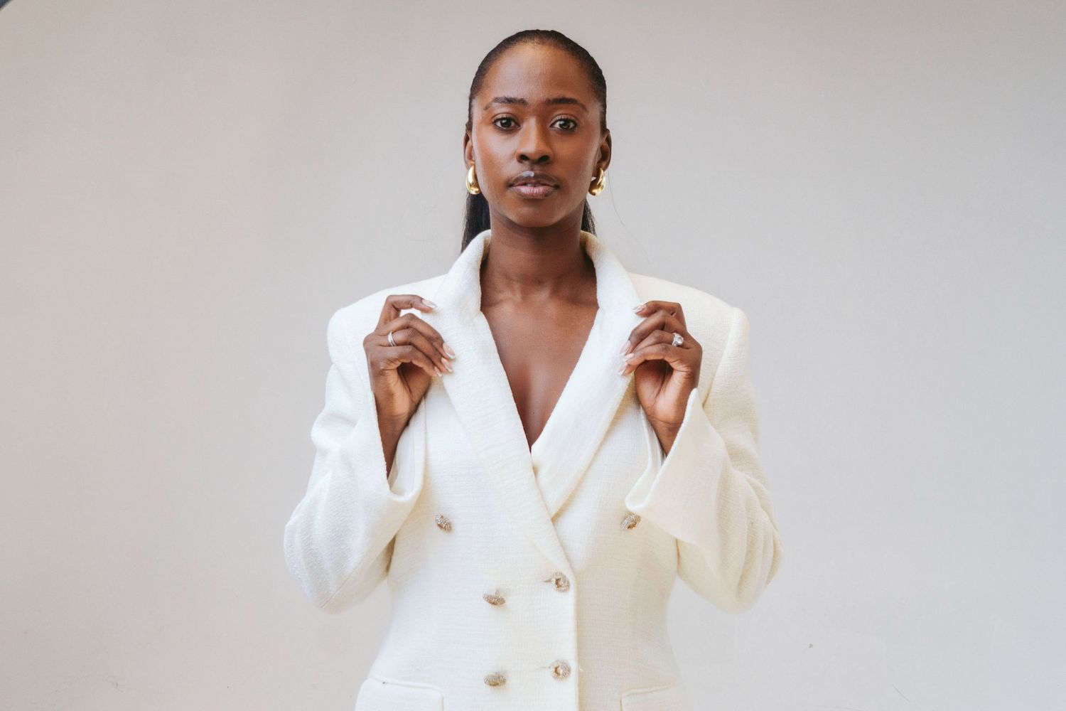 A person wearing a crisp white blazer poses against a light gray background in a fashion-forward portrait series.