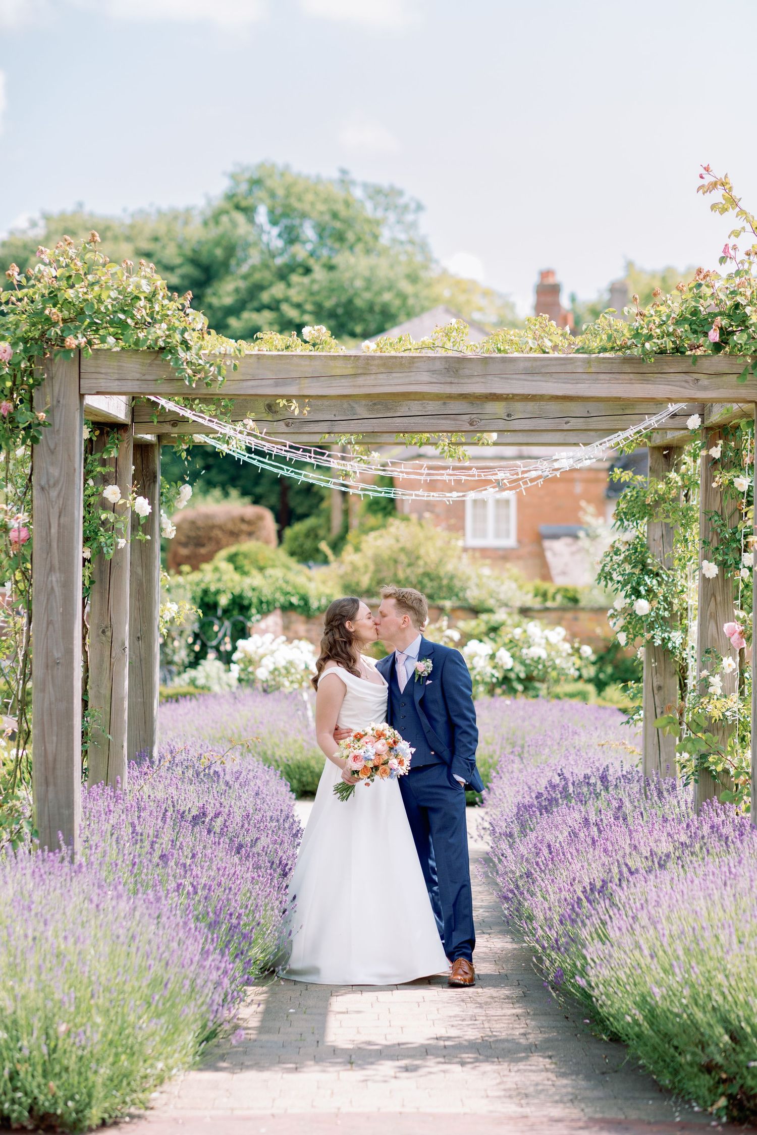 A romantic garden scene with a wooden pergola over a path lined with blooming lavender and climbing roses.