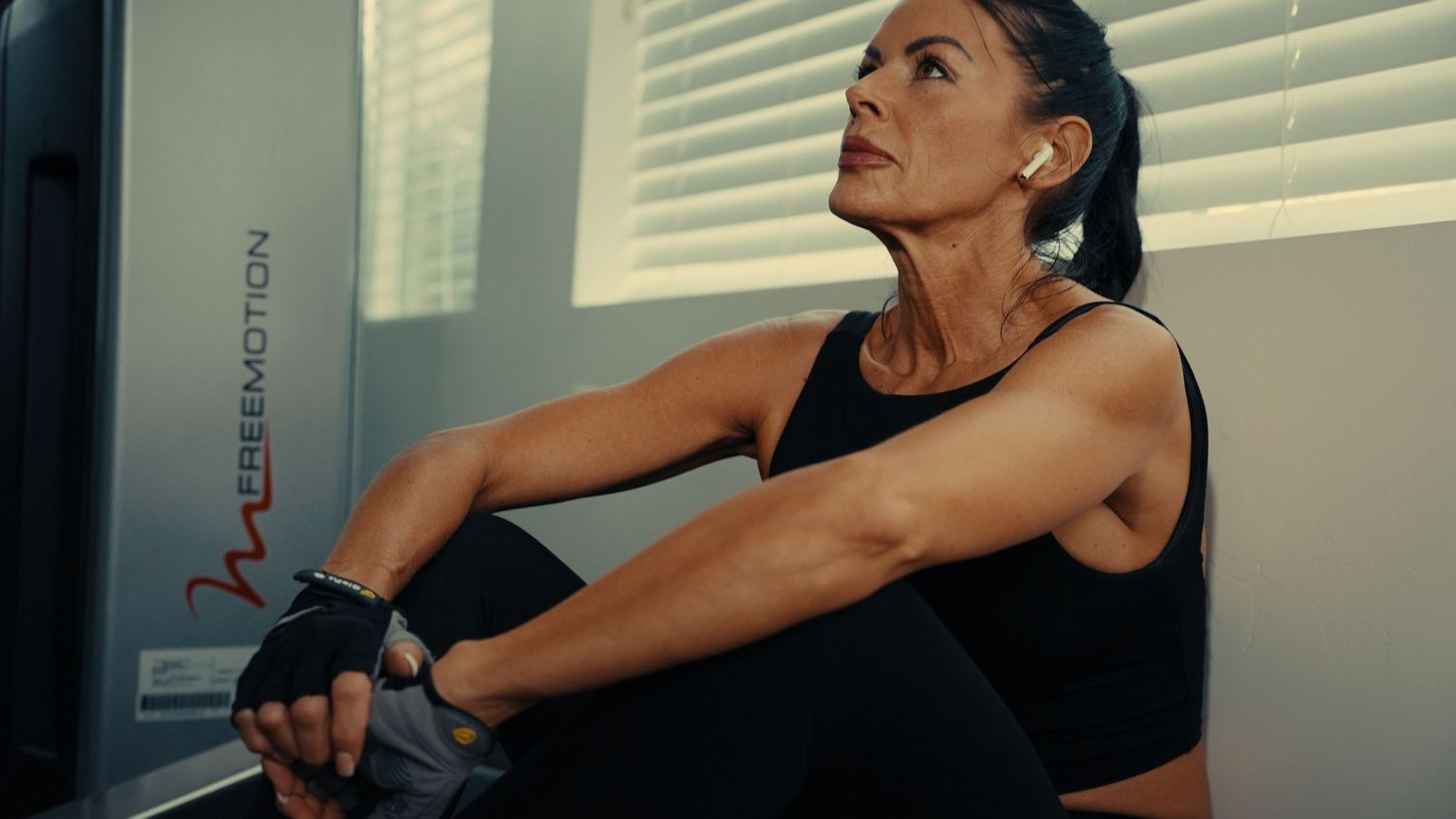 Person in black workout attire performs stretching exercises in front of window blinds.