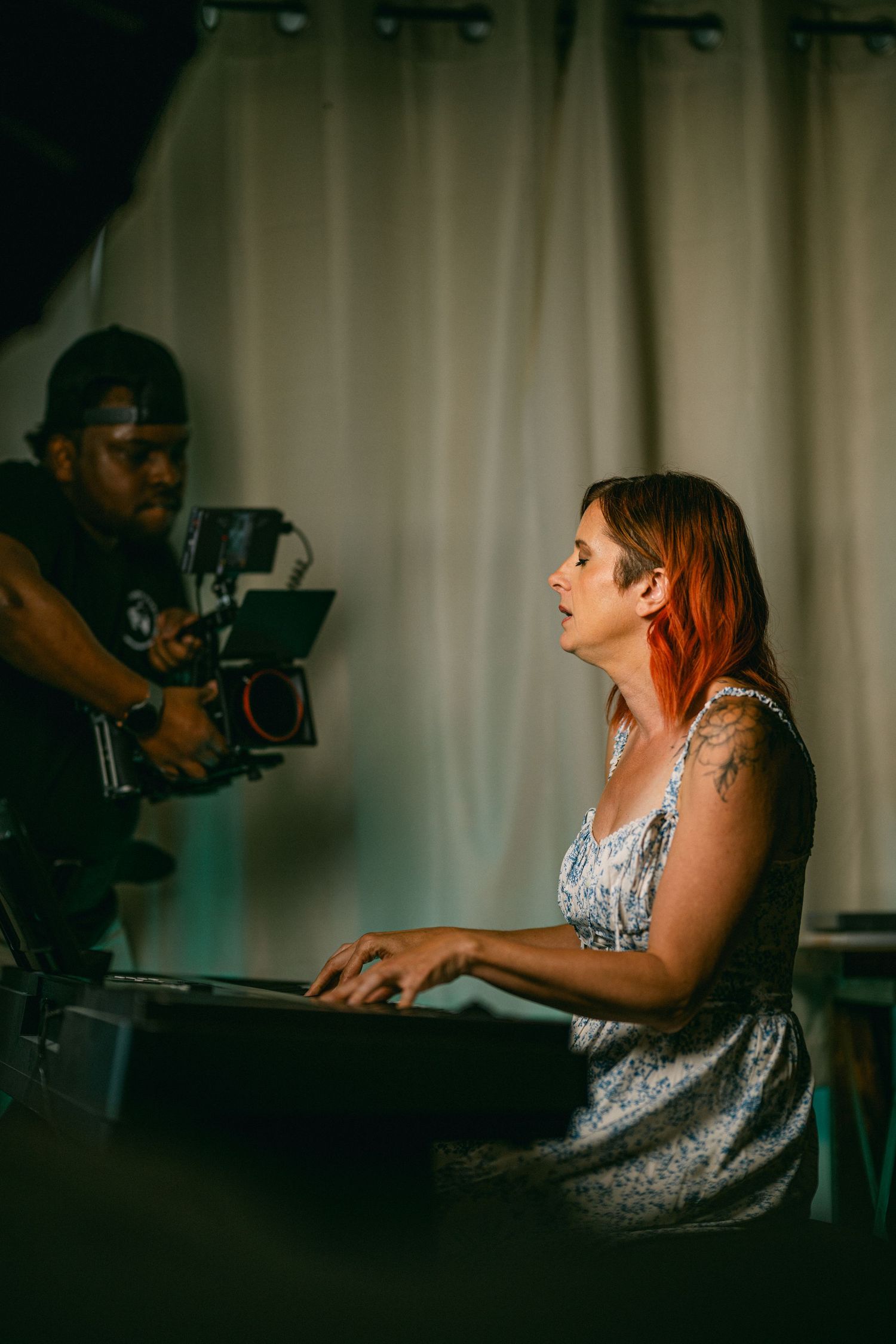 Musician performs at piano while being filmed in dramatic lighting.