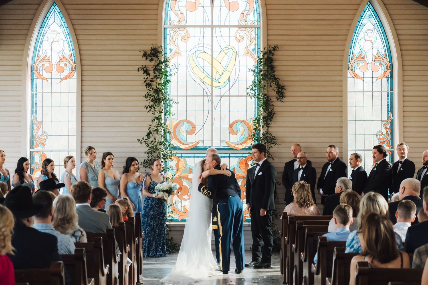 A wedding ceremony taking place inside a chapel with beautiful stained glass windows and floral decorations.