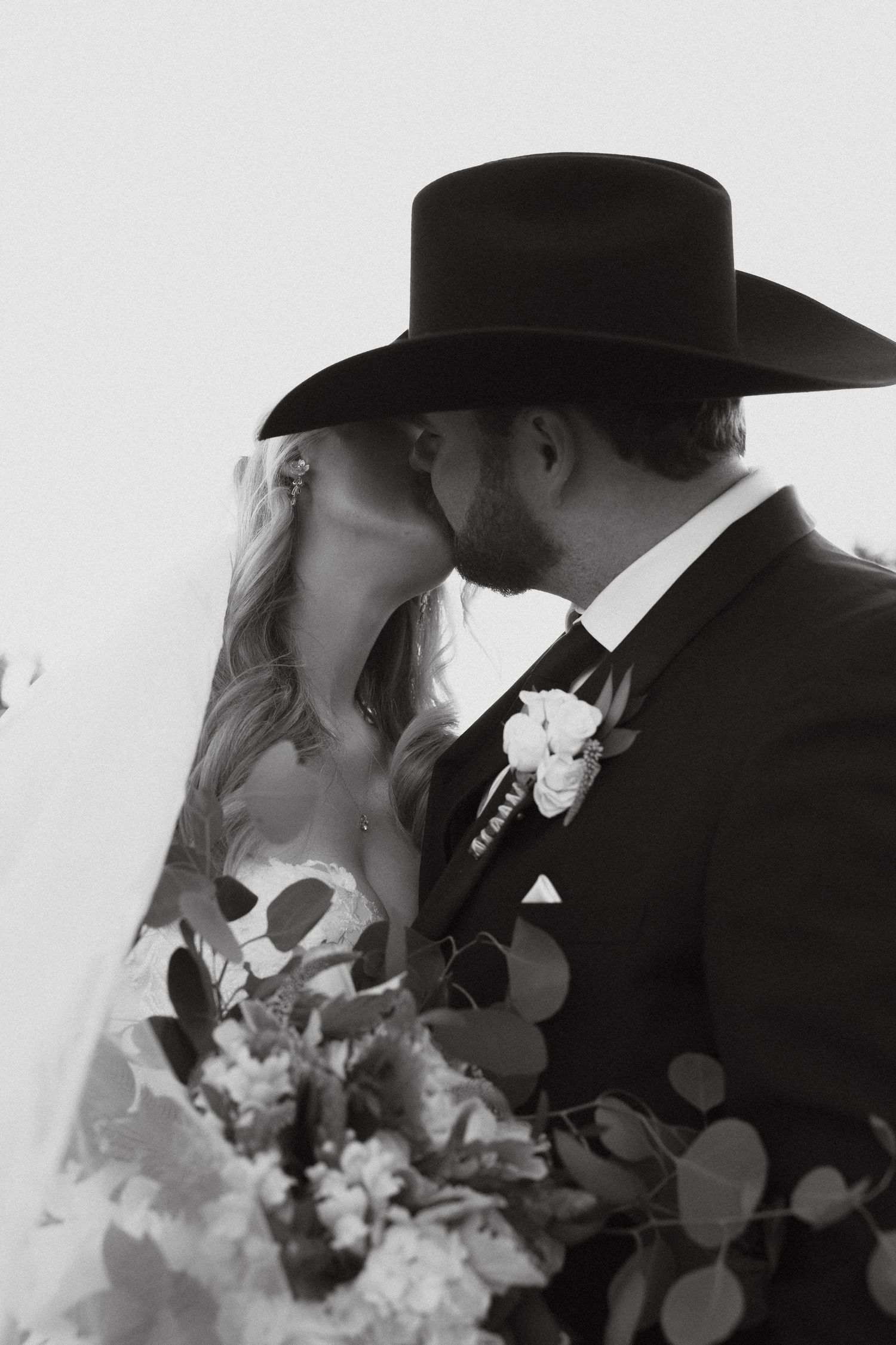 Romantic black and white silhouette of newlyweds in cowboy hats sharing an intimate kiss.