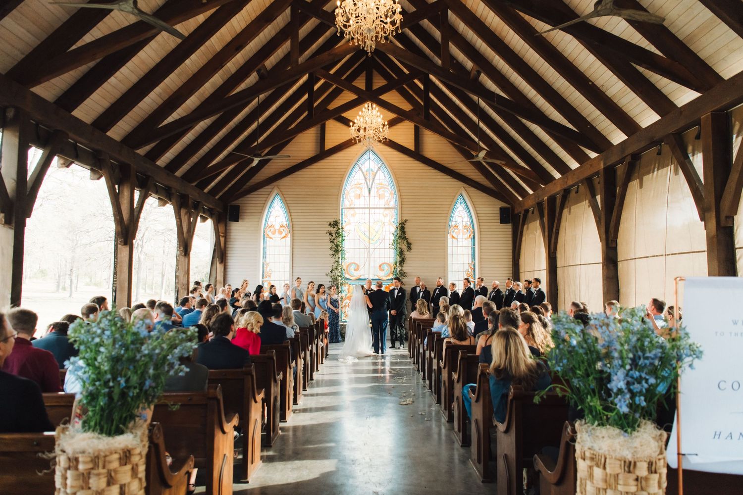 Long wooden church hall with exposed beams decorated with floral arrangements and set up for a wedding ceremony.