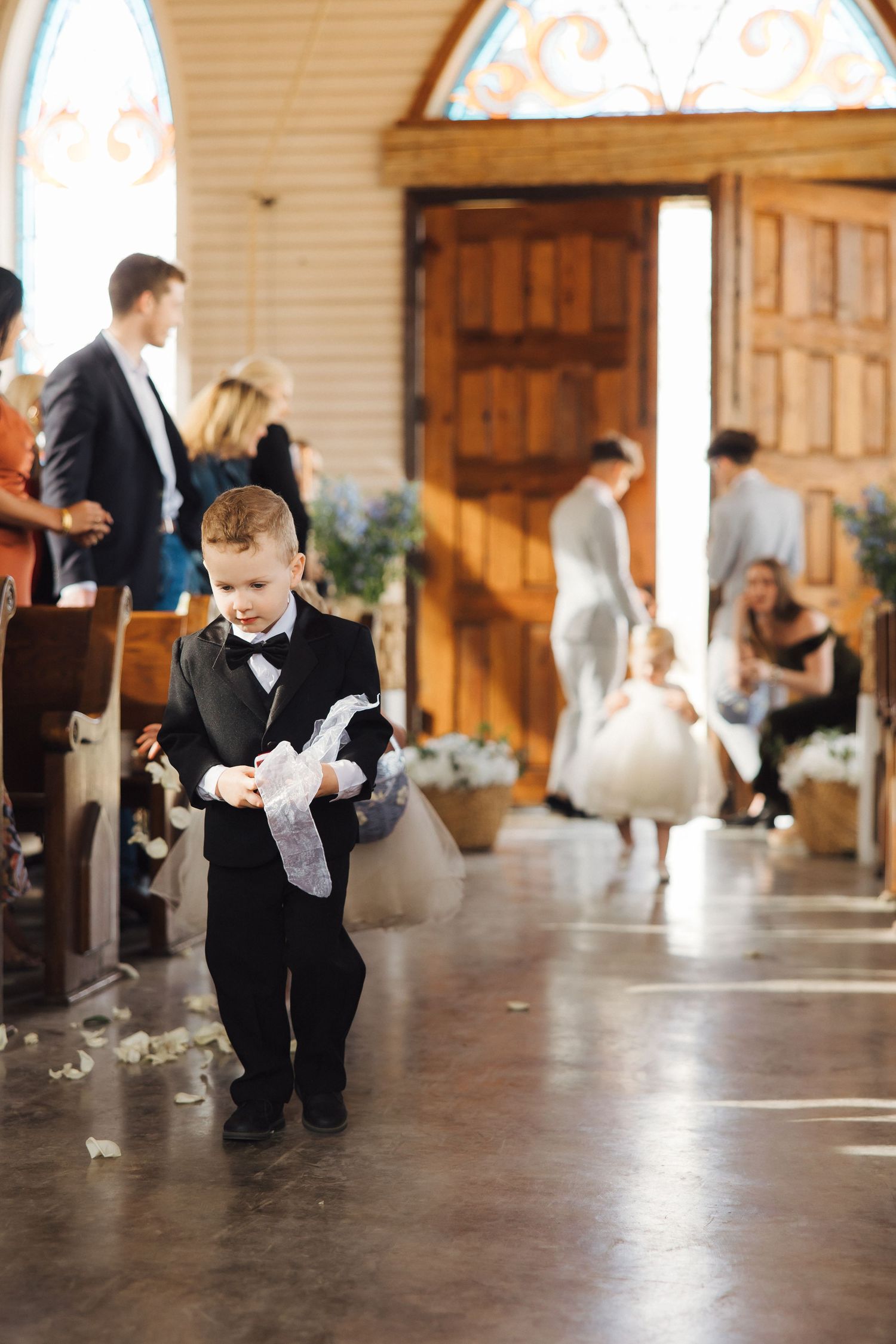 A young ring bearer in formal attire plays on the floor during a wedding celebration.