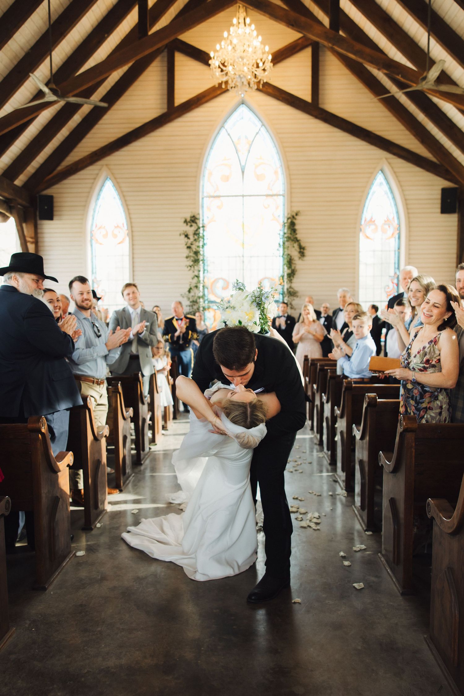 Wedding guests celebrate during a reception inside a rustic chapel with exposed wooden beams.
