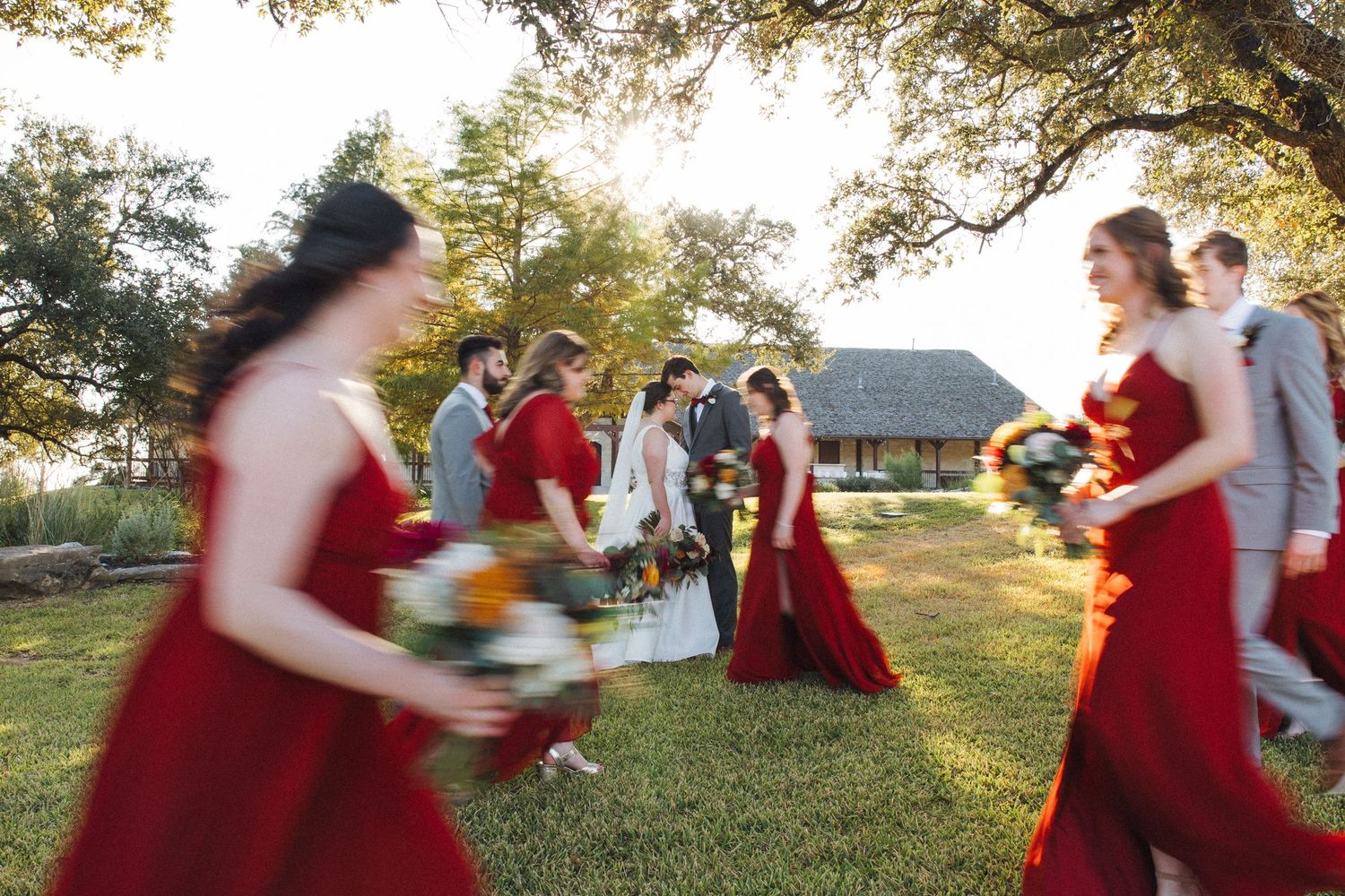 Several people in red and white outfits dance and spin together in a sunny outdoor garden setting during golden hour.