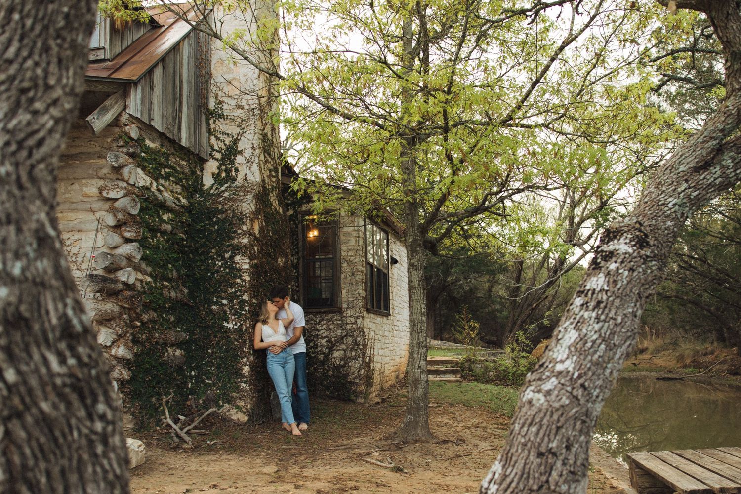 A rustic stone cottage nestled among trees with someone standing by the entrance.