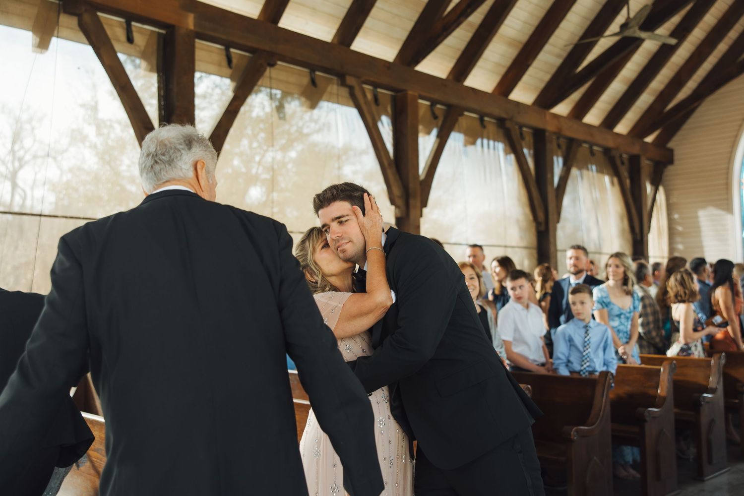 An emotional moment during a wedding ceremony in a rustic venue with wooden beams and gathered guests in the pews.