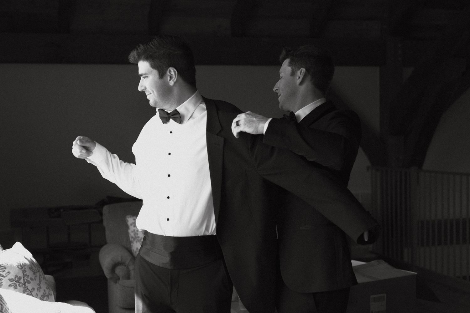 Two brothers, one is helping his brother into his jacket getting ready for his wedding day.