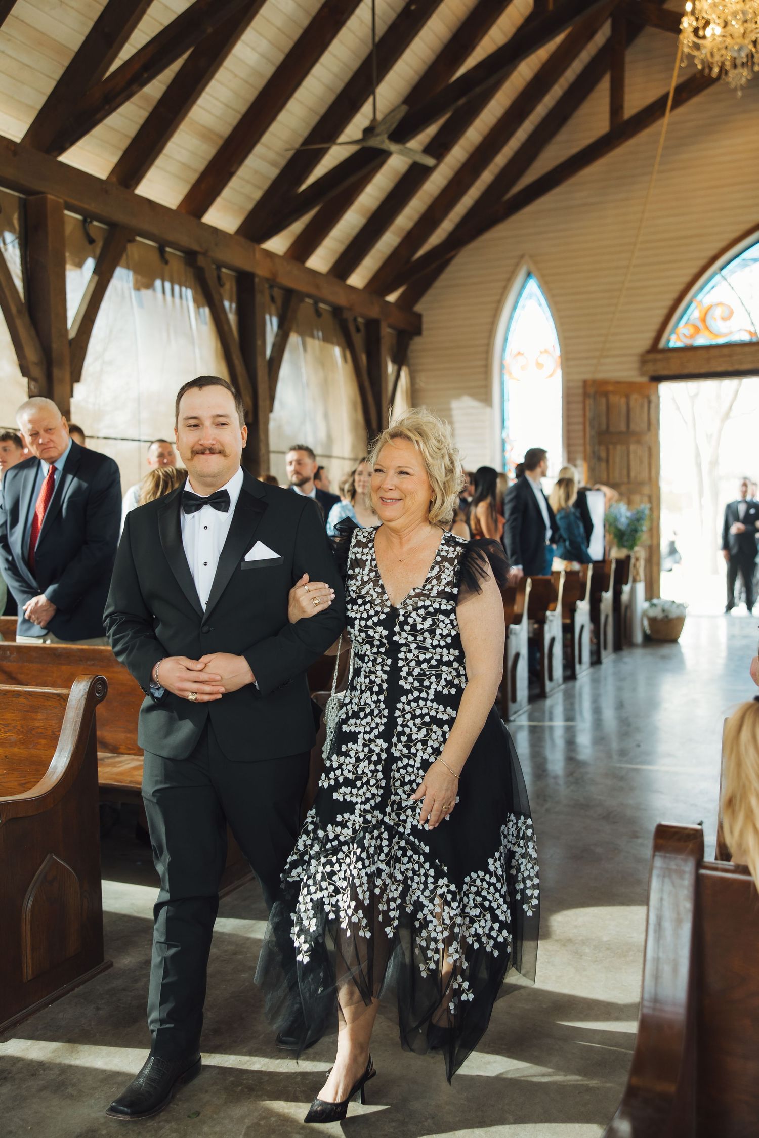 Elegant wedding ceremony inside a chapel with exposed wooden beams and stained glass windows.