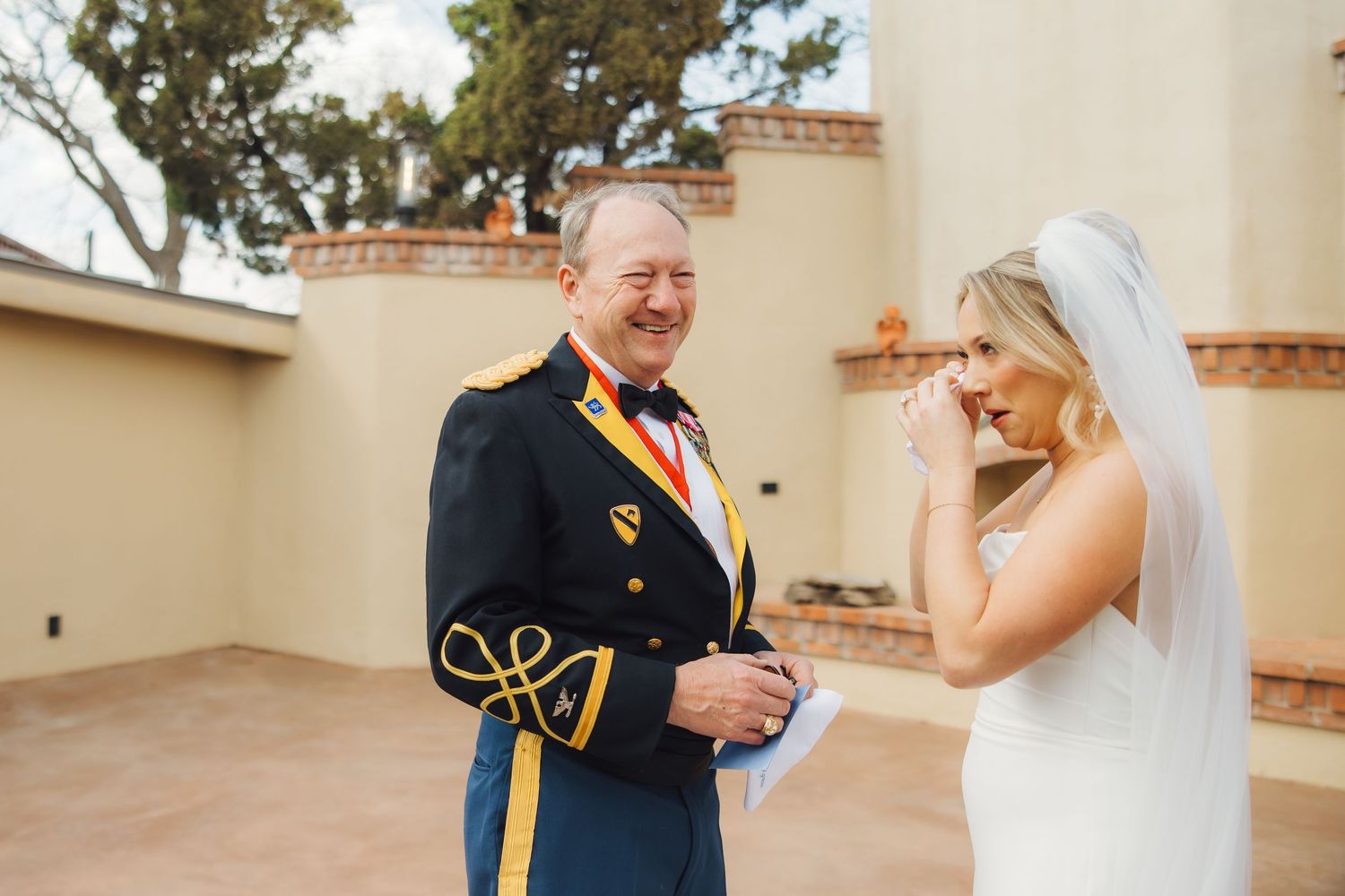 An emotional first look between a military officer in dress uniform and a bride in a white wedding gown and veil.