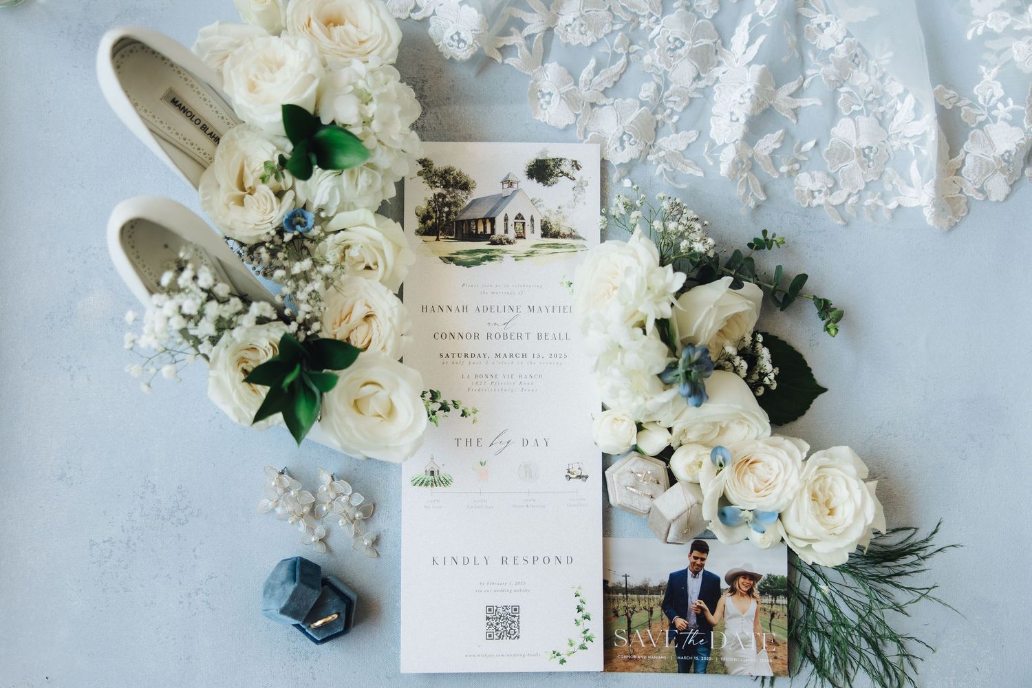 Flat lay of wedding details including invitation, white shoes, roses and delicate lace accents.