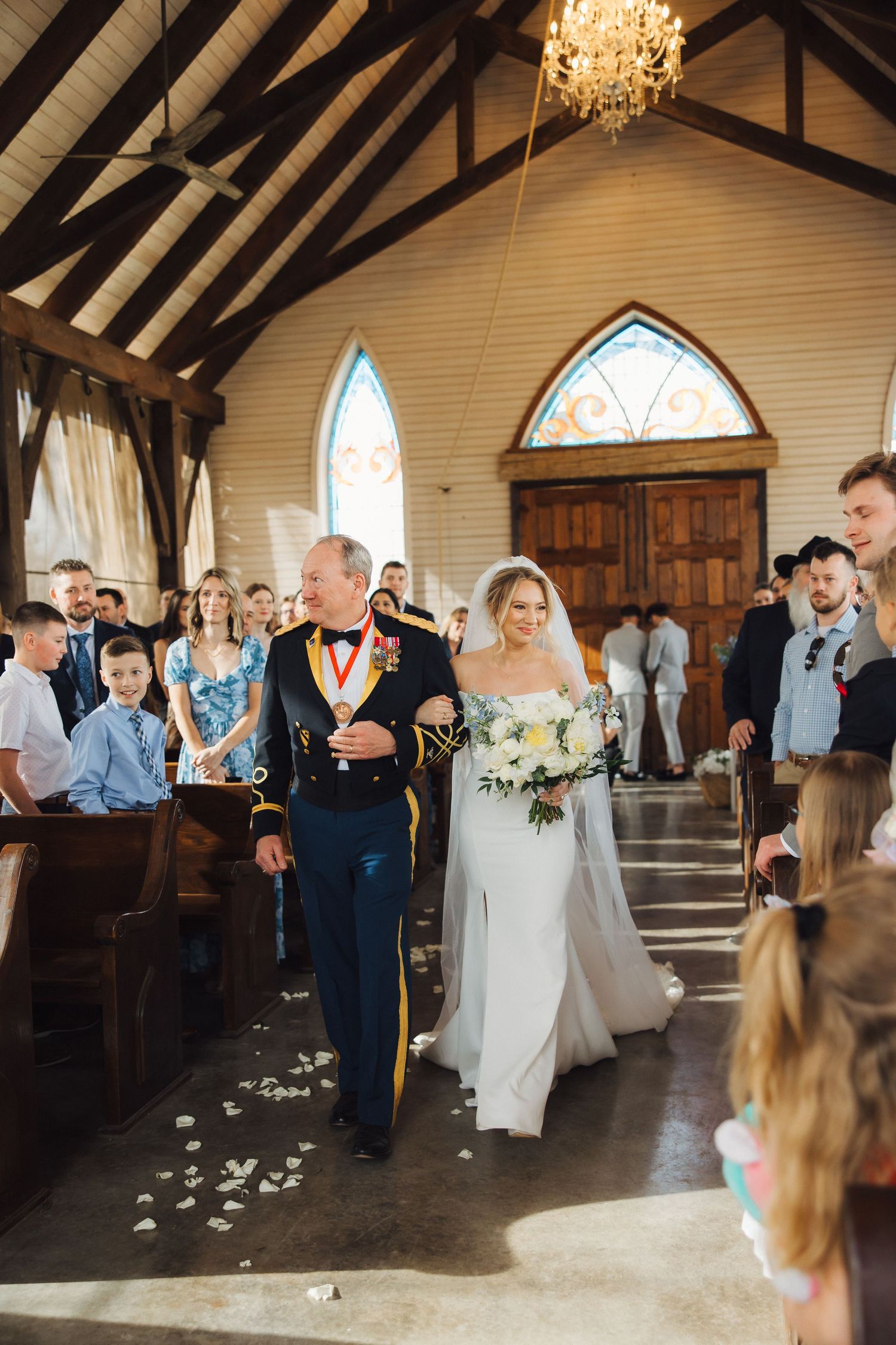 Wedding party processes down the aisle in a rustic chapel with exposed wooden beams and stained glass windows.