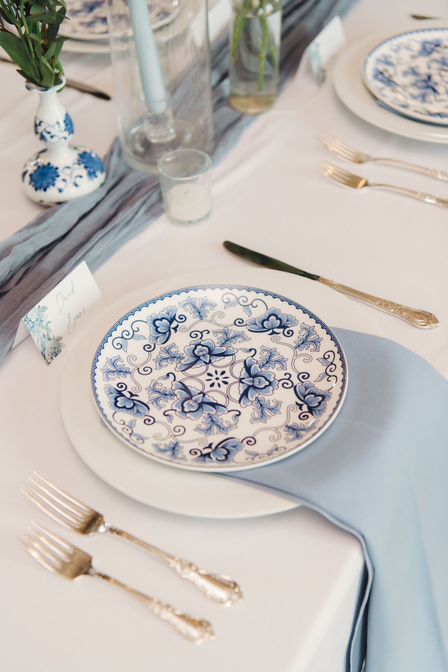 Blue and white china plate with delicate floral pattern set with gold cutlery and light blue napkin.