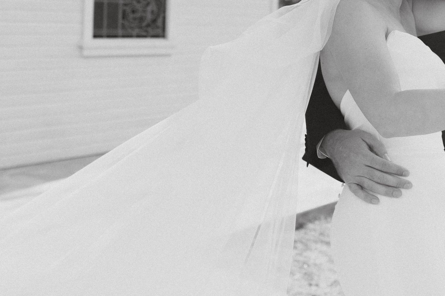 A close-up detail shot of a flowing white wedding dress skirt being adjusted during a fitting or preparation.