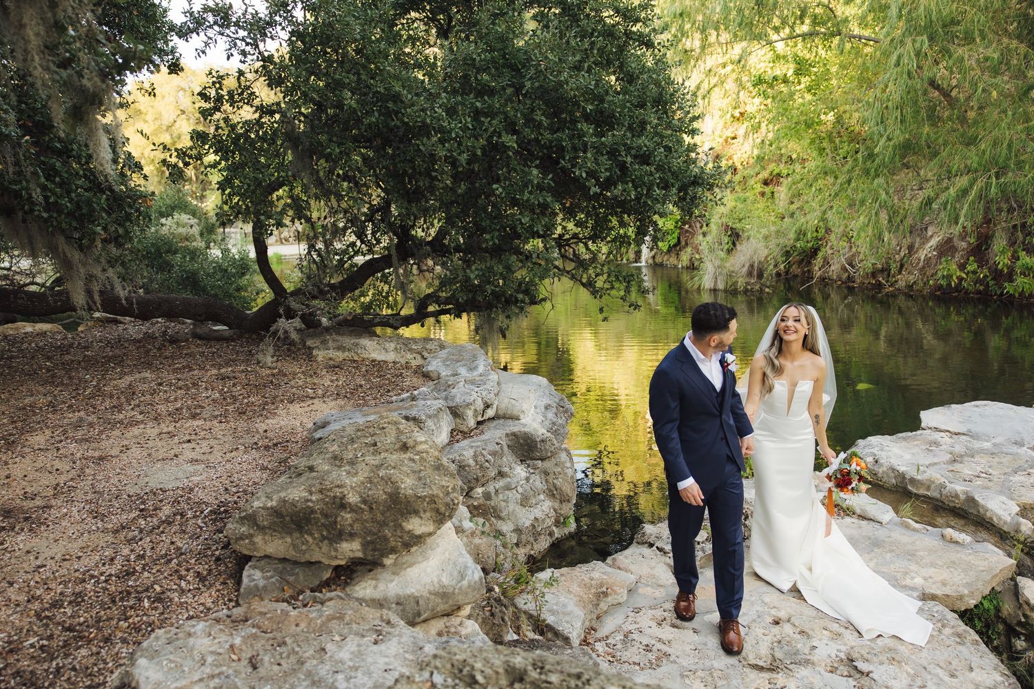 A romantic wedding photoshoot sequence showing a couple walking along a scenic creek bed in nature.