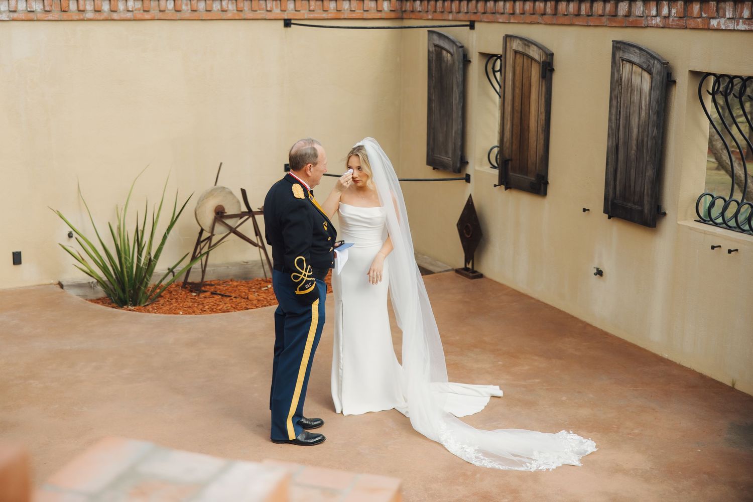 A couple shares a romantic moment on a stone patio, with the person in military dress uniform facing their partner in white.