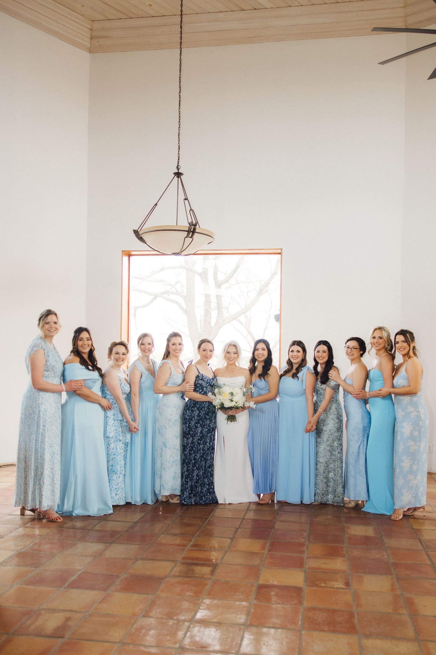 Bridesmaids in light blue dresses pose together in a line at an indoor venue.
