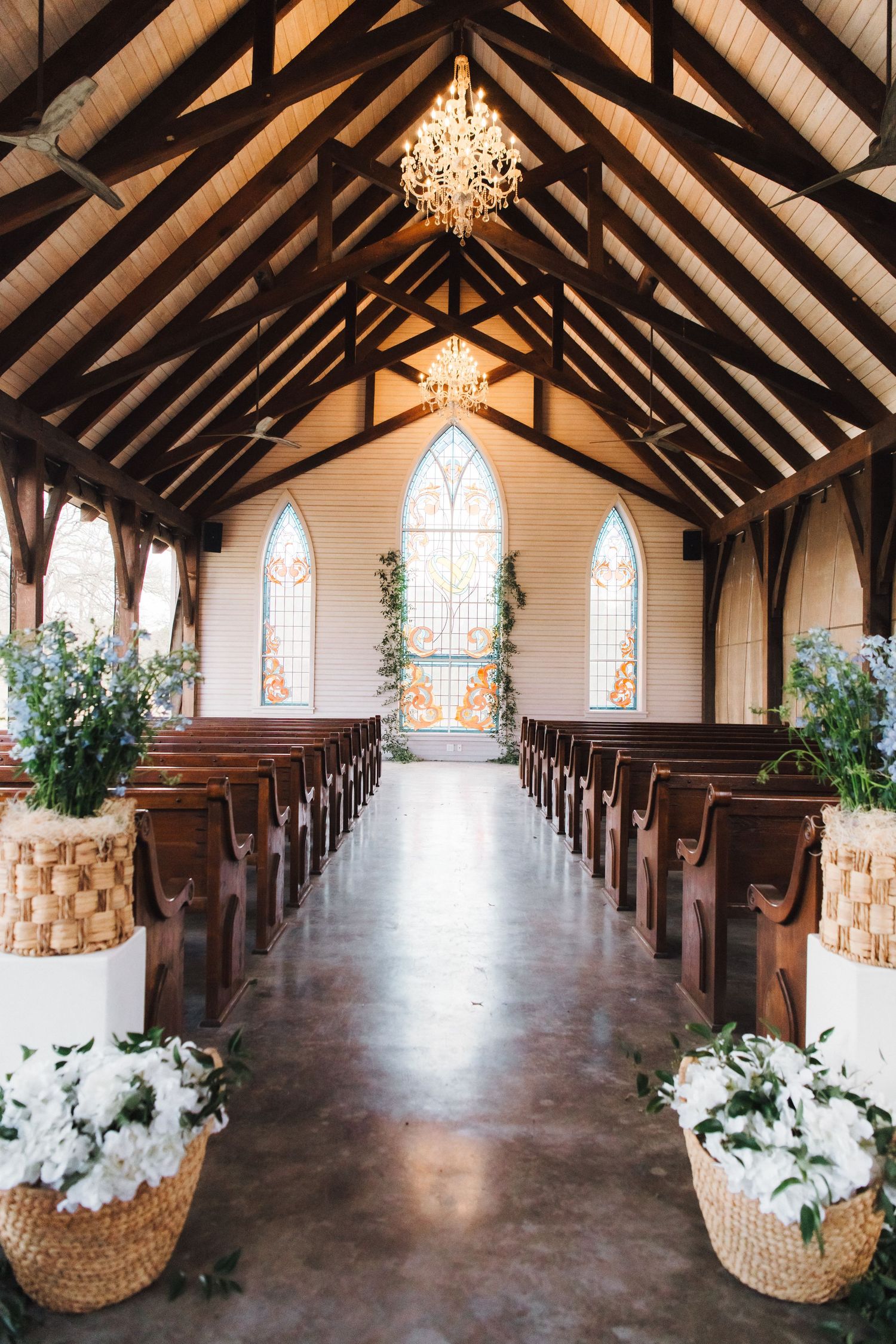 Chapel interior with wooden beam ceiling, stained glass windows and flower-decorated aisle.