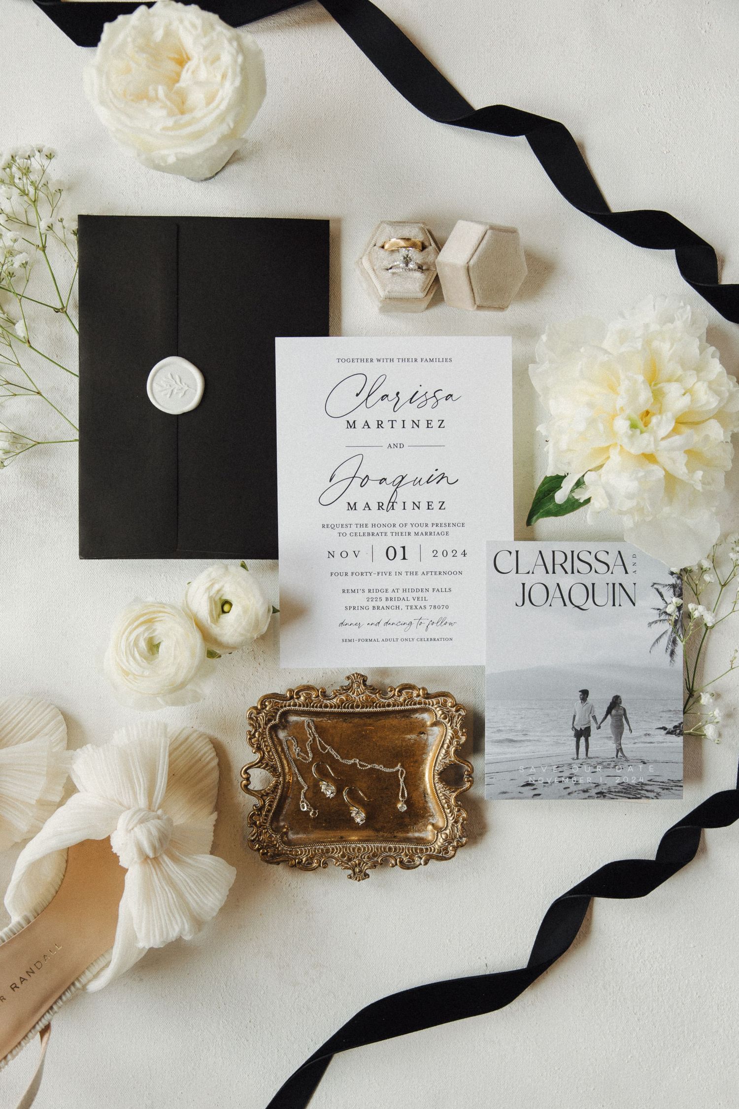 Elegant wedding stationery flatlay with black and white invitations, white flowers, vintage gold frame, and silk ribbon details.
