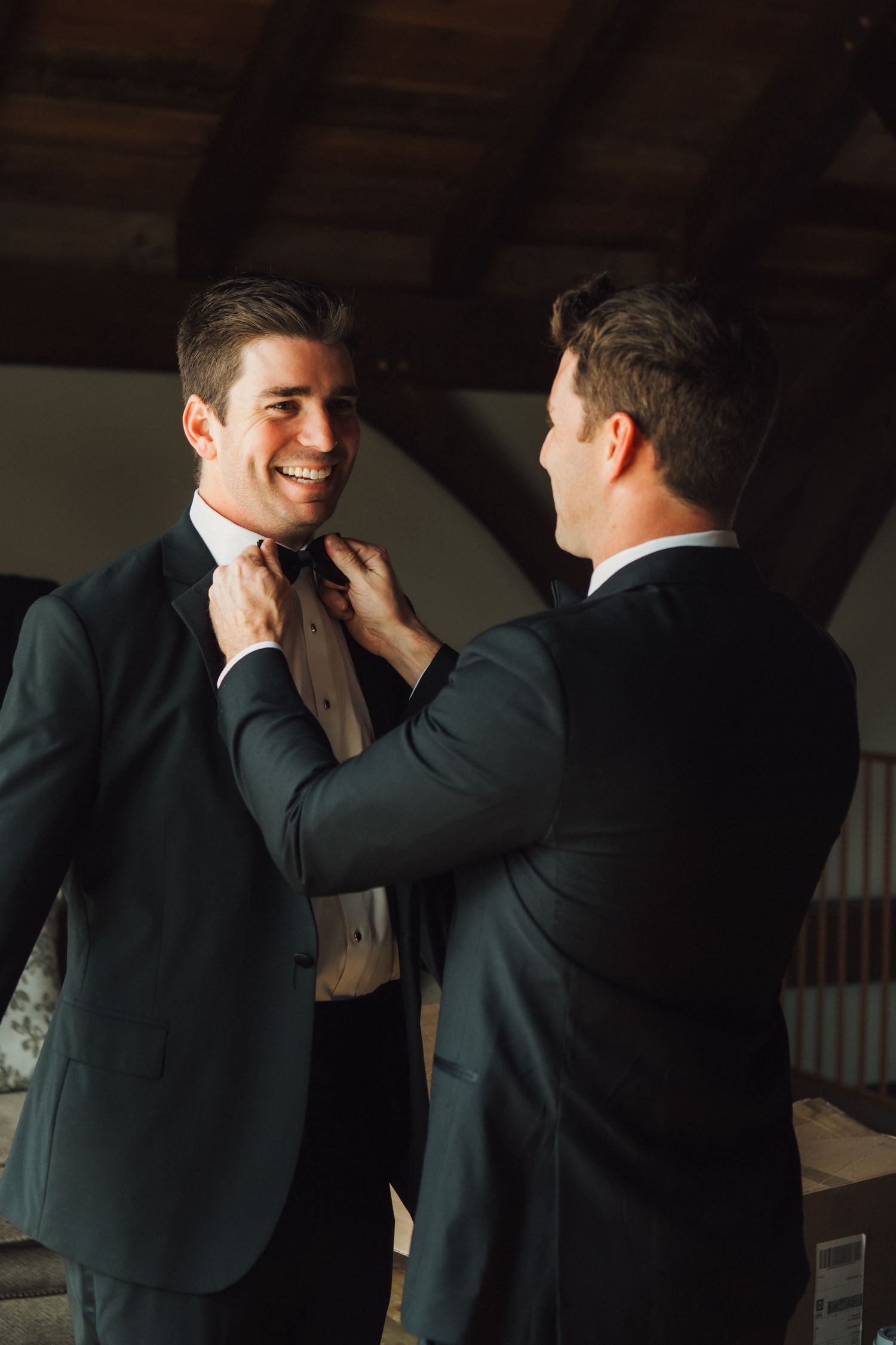 Two people in formal attire adjusting a bow tie during preparation.