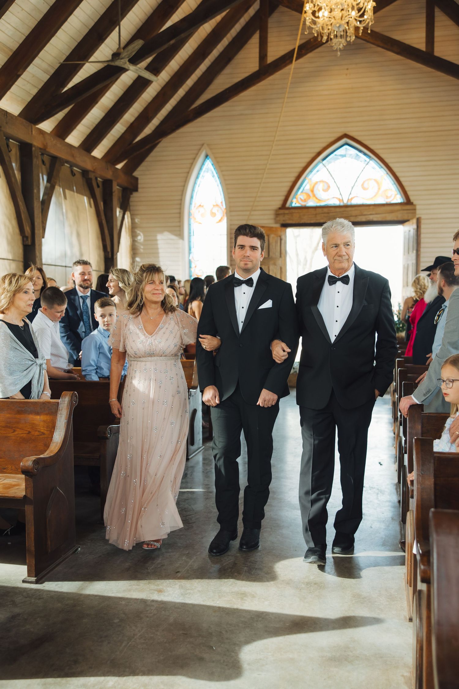 Wedding party walking down the aisle in a rustic chapel with exposed beams and stained glass windows.