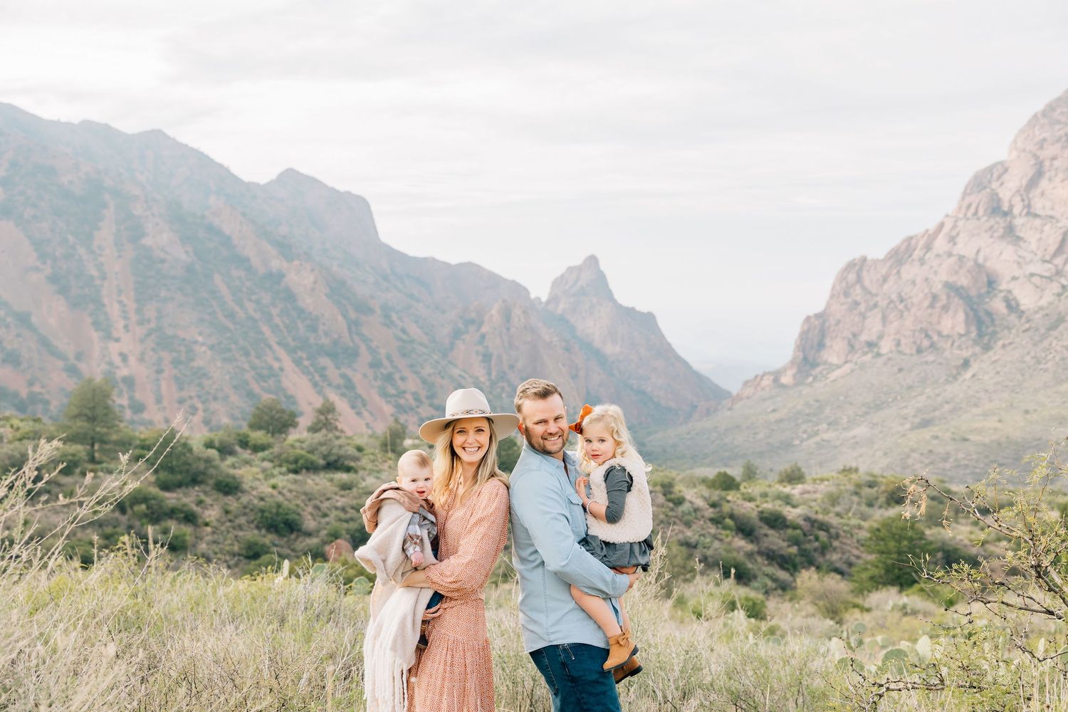 A group stands among desert mountains and cacti in a scenic outdoor photoshoot at golden hour.