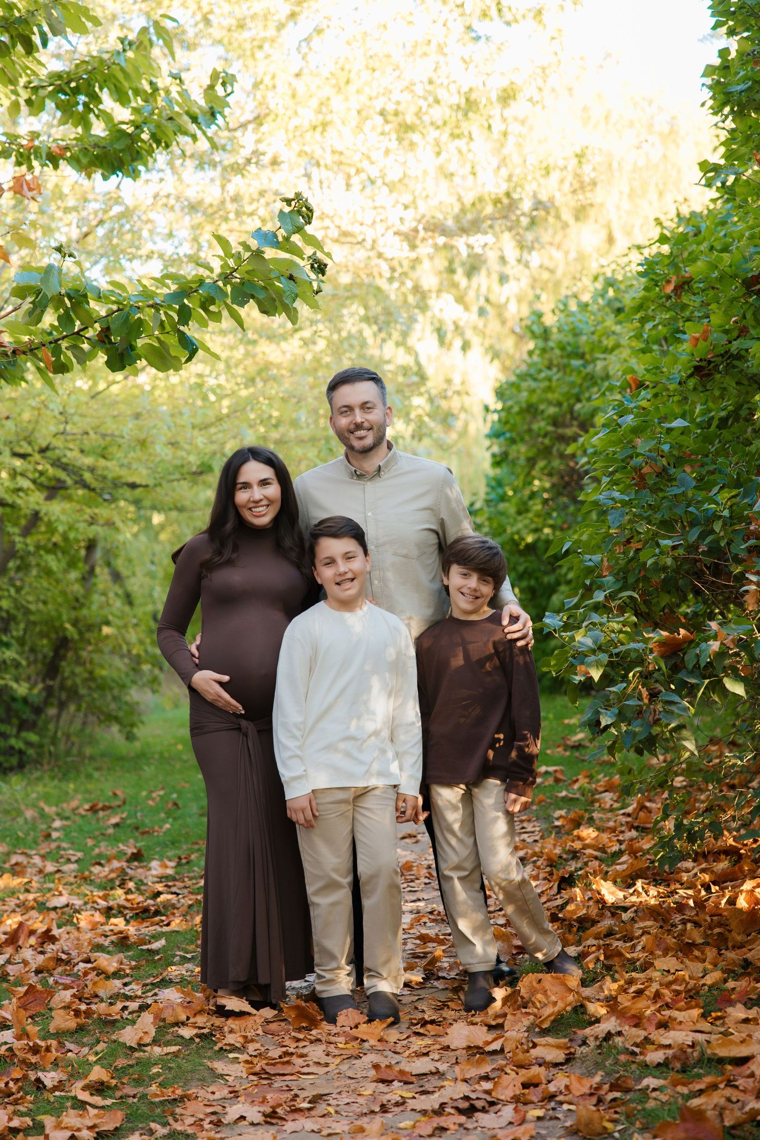Happy family of four with pregnant mother posing in autumn park with colorful fallen leaves.