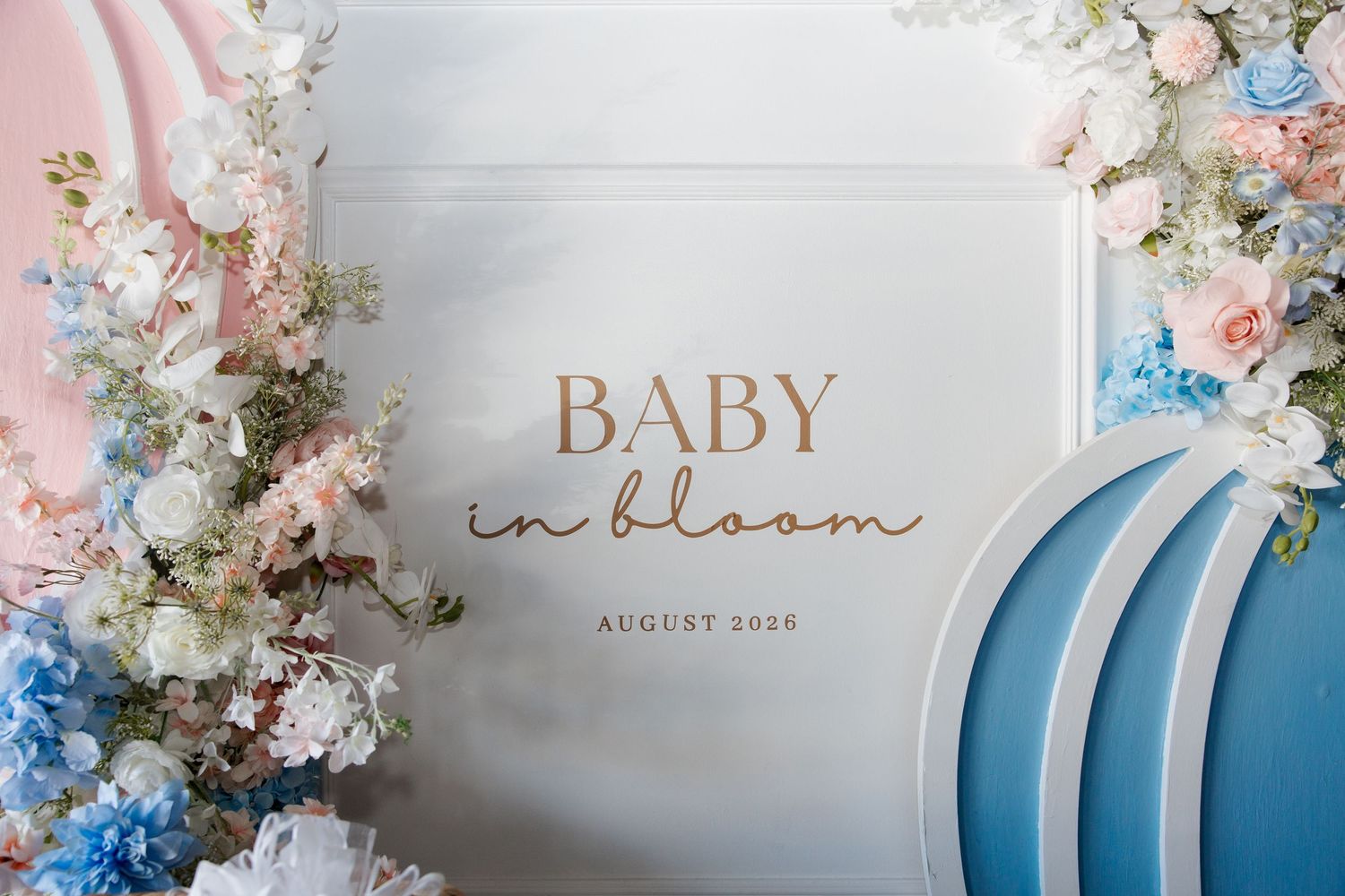 Baby in Bloom baby shower backdrop with pink and blue floral arrangements and decorative blue arches, August 2026.