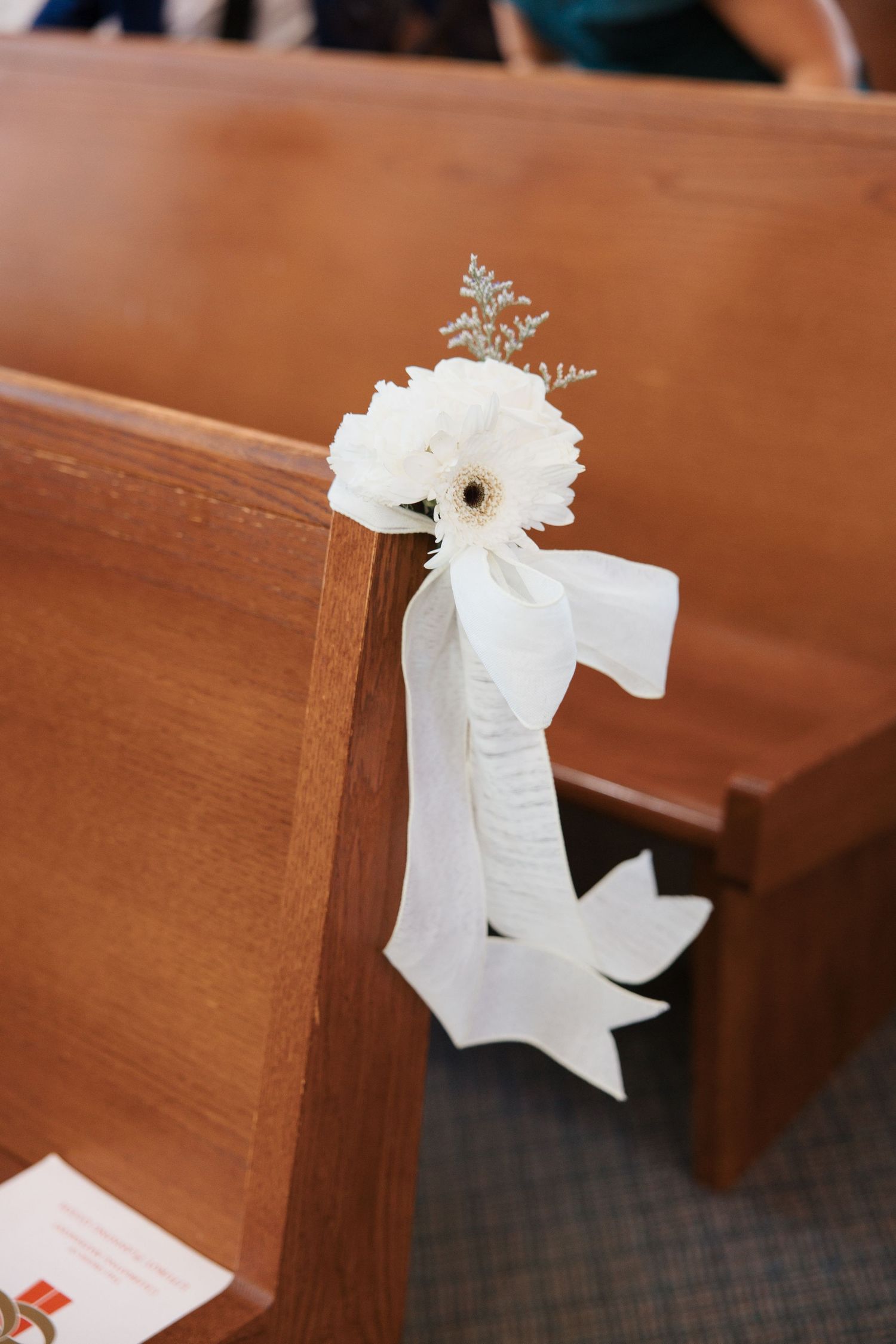 White floral pew decoration with ribbon bow on wooden church bench for wedding ceremony.