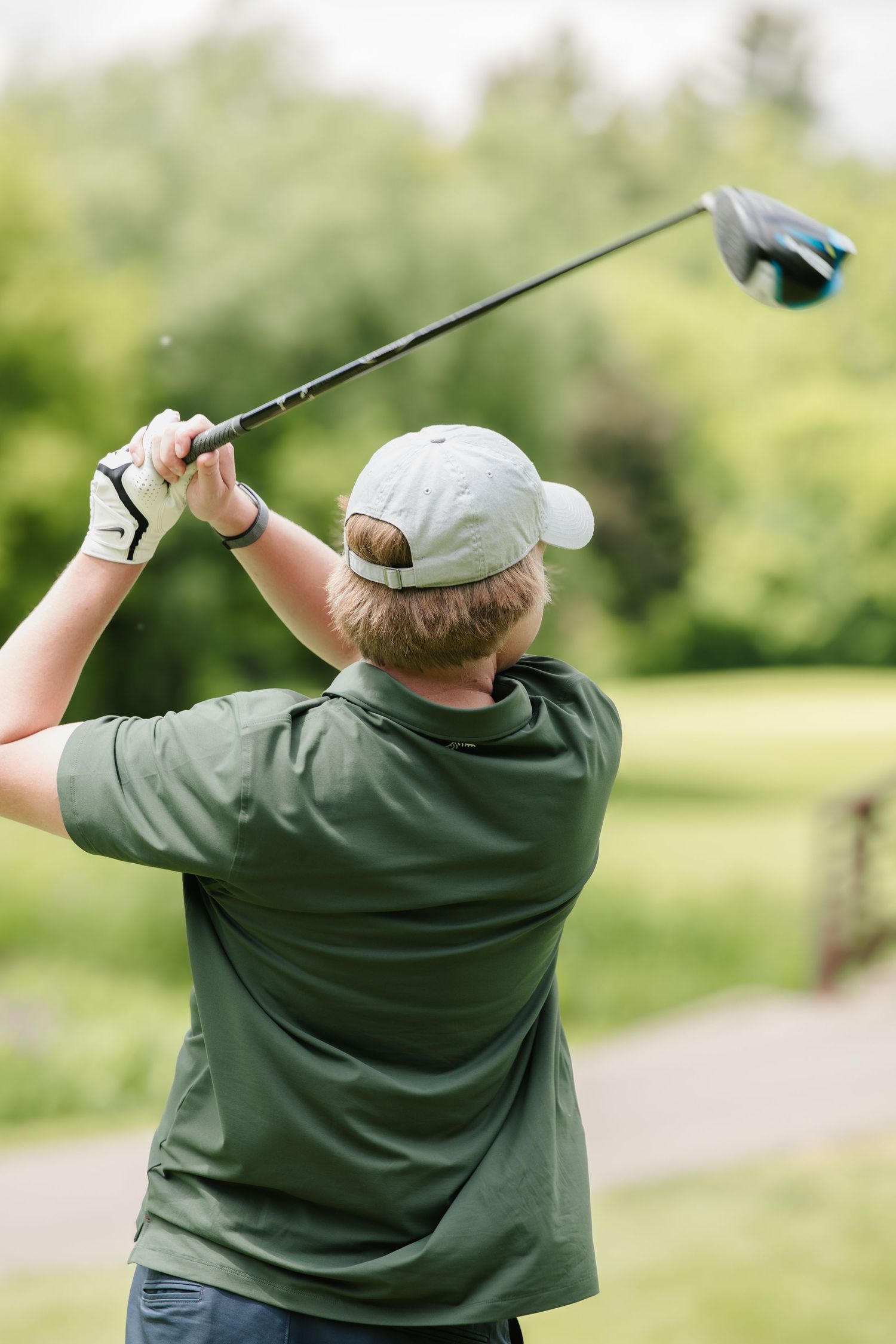 Golfer in green polo and cap completing a driver swing follow-through on a lush green golf course.