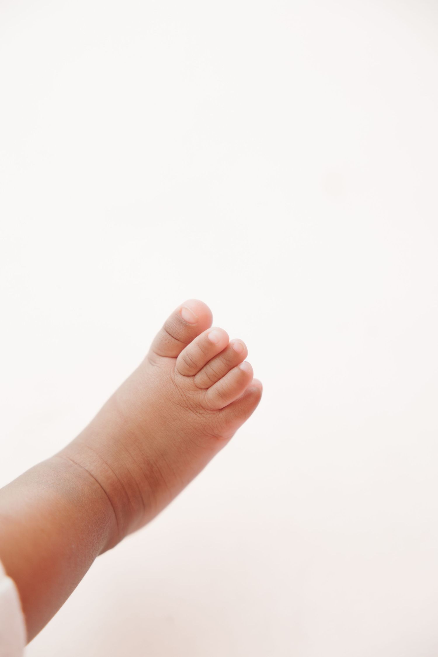 Close-up of a tiny newborn baby foot with delicate toes against a soft white background.