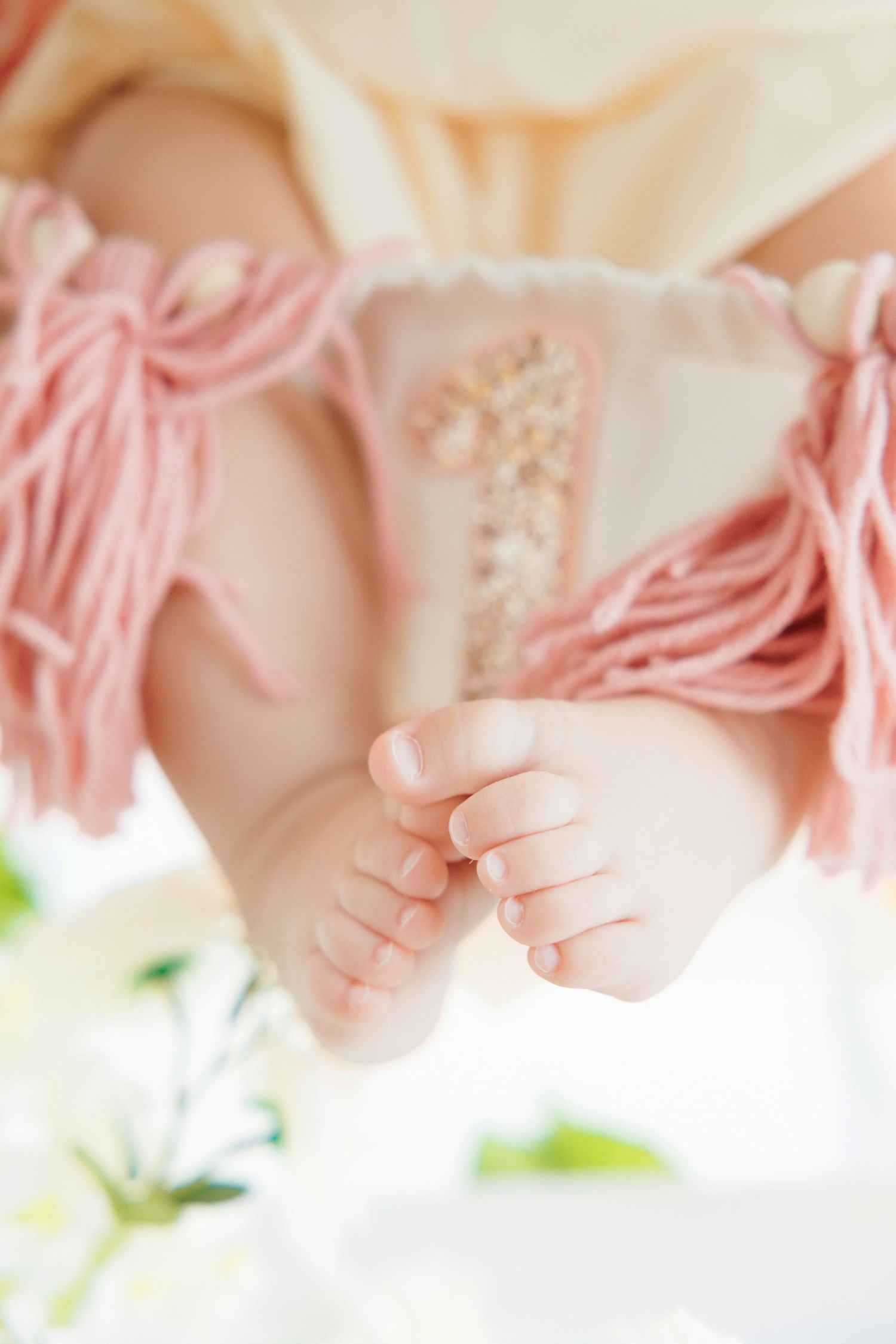 Close-up of tiny newborn baby feet with pink fringe outfit detail.