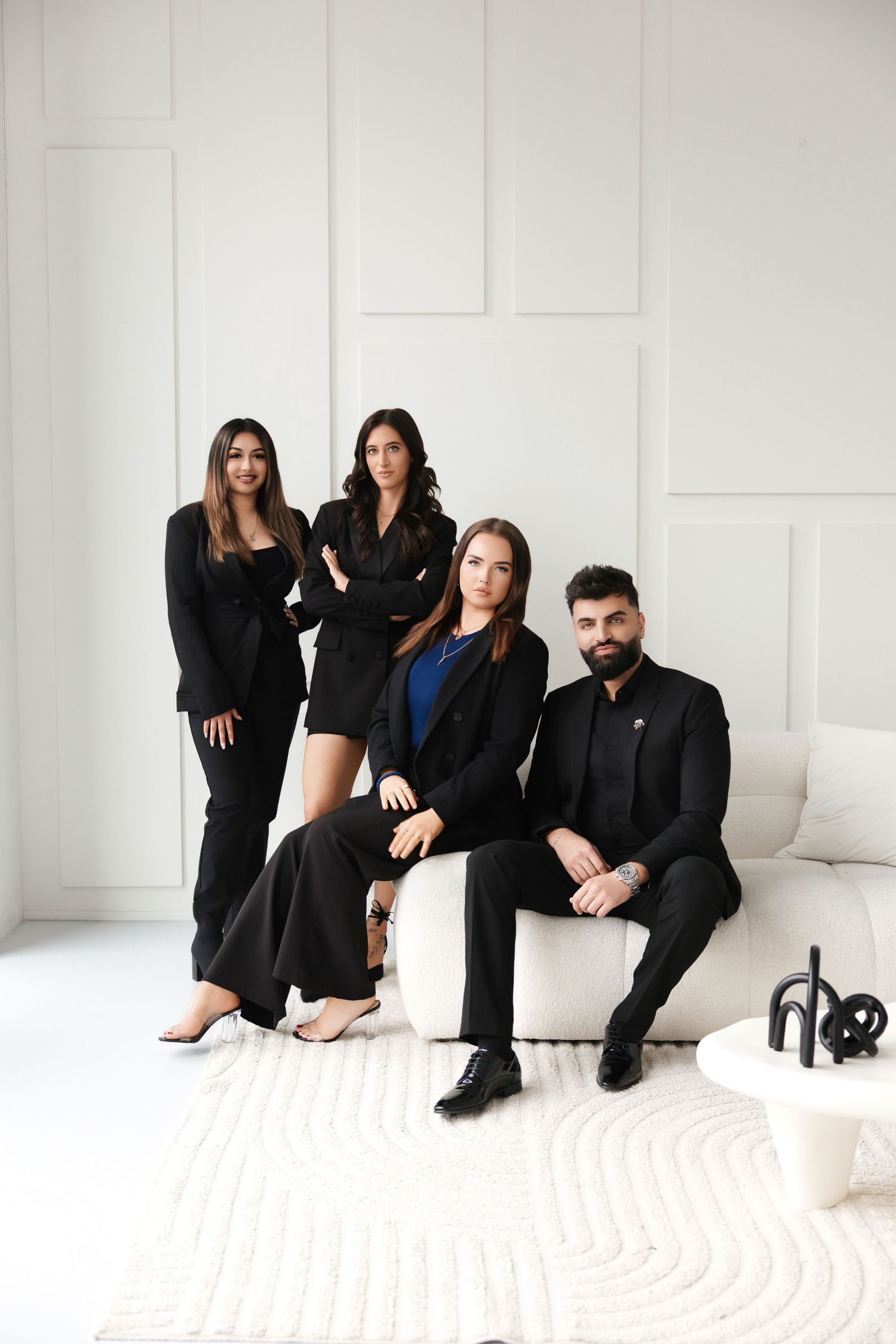 Four elegantly dressed professionals in black attire pose in a modern white interior setting.