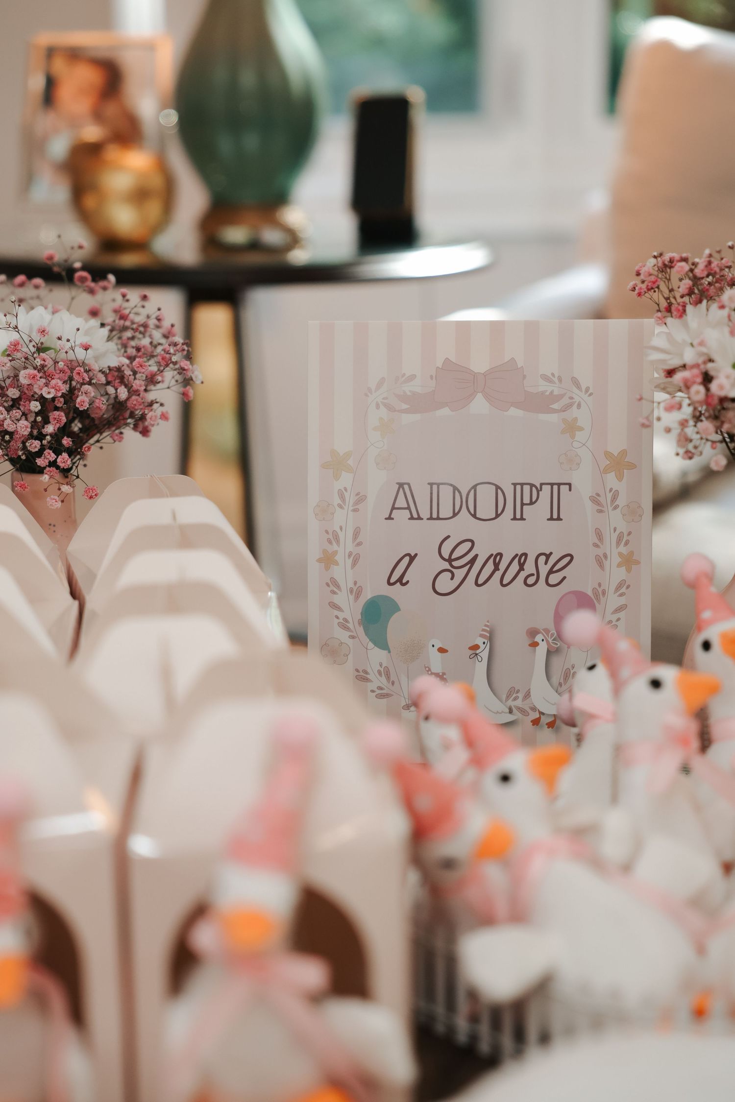 Adopt a Goose baby shower table display with plush goose toys, white favor boxes, and pink floral decorations.