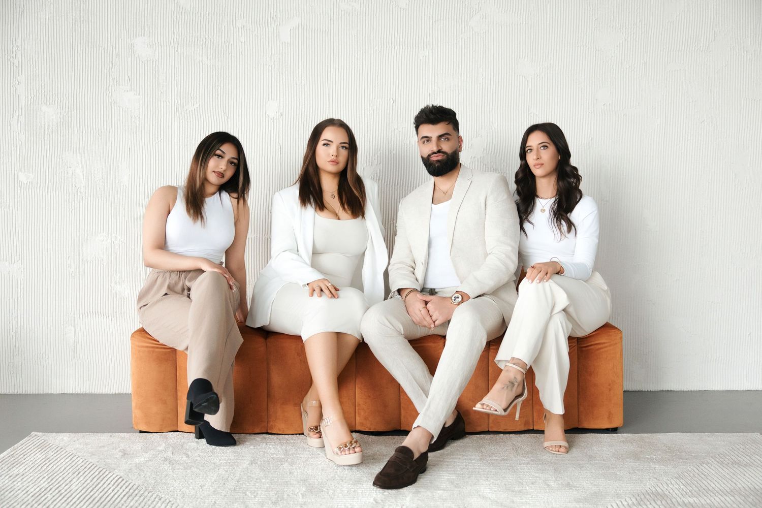 Four professionals in coordinated neutral beige and white outfits sit together on an orange bench.