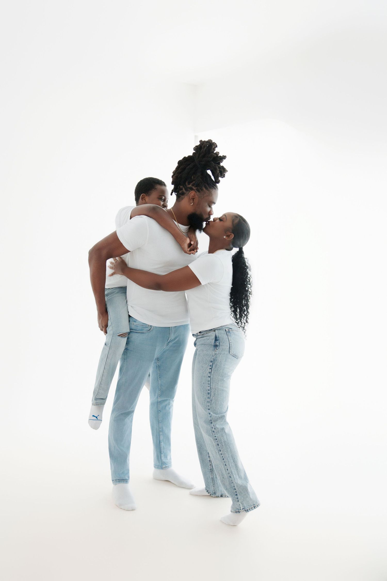 Happy African American family in matching white tees and jeans embracing together against white background.