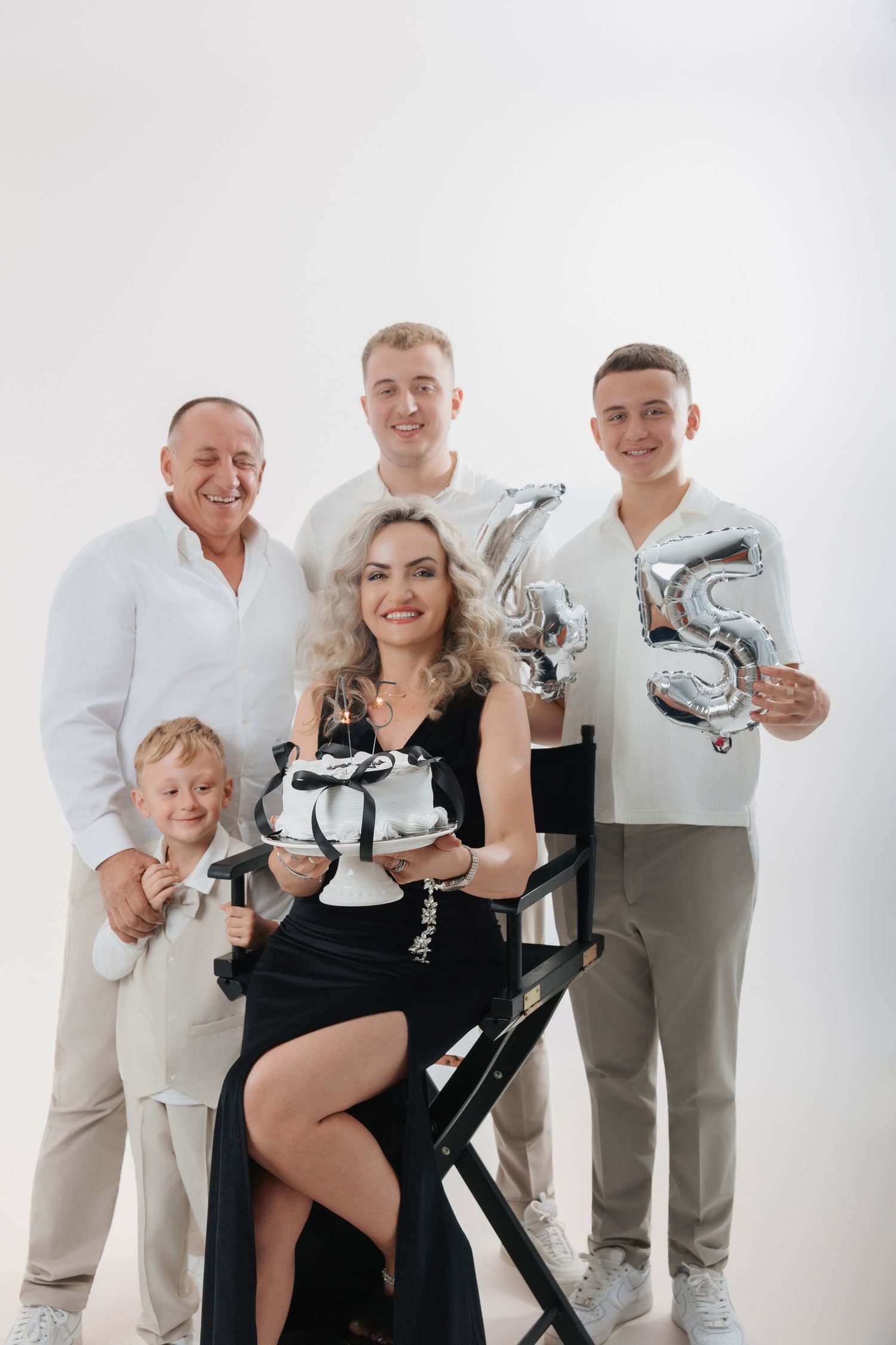 Family of five celebrating a 35th birthday with white cake and silver balloon numbers on white background.