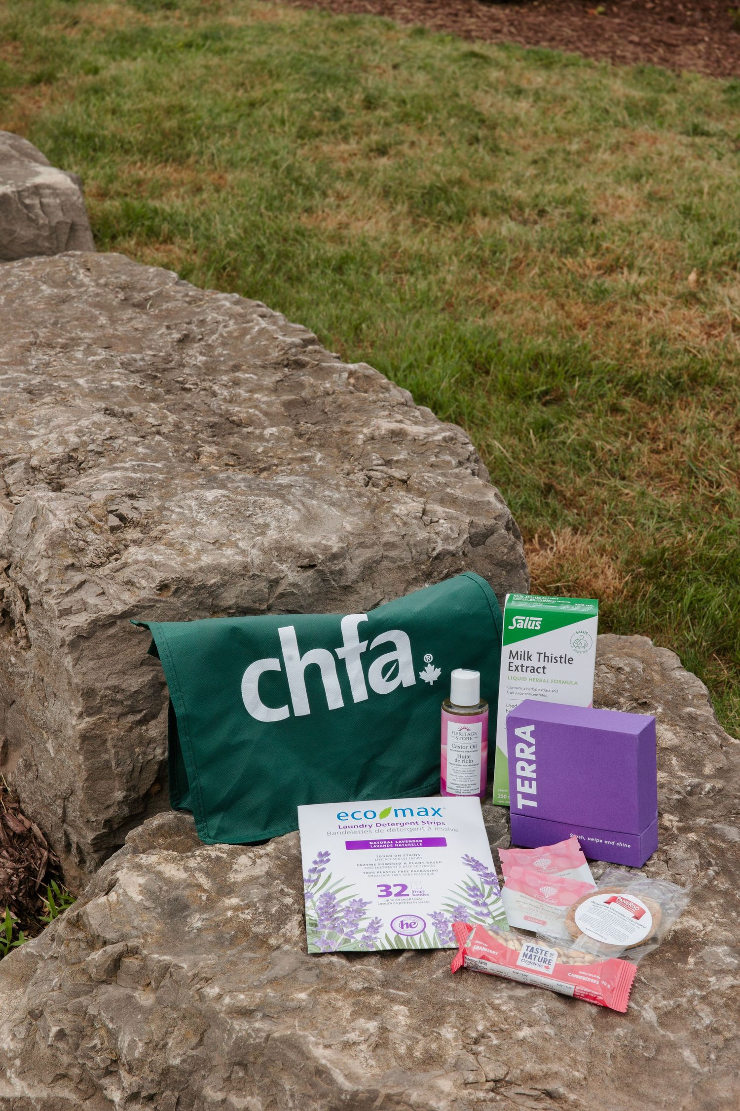 CHFA green tote bag displayed on rocks outdoors with eco-max, Terra, and Salus Milk Thistle natural health products.