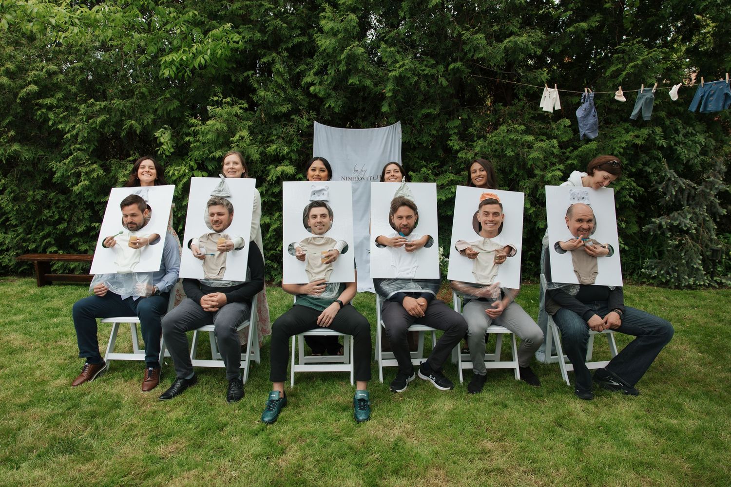 Group of people sitting outdoors holding large printed photos in a backyard setting.
