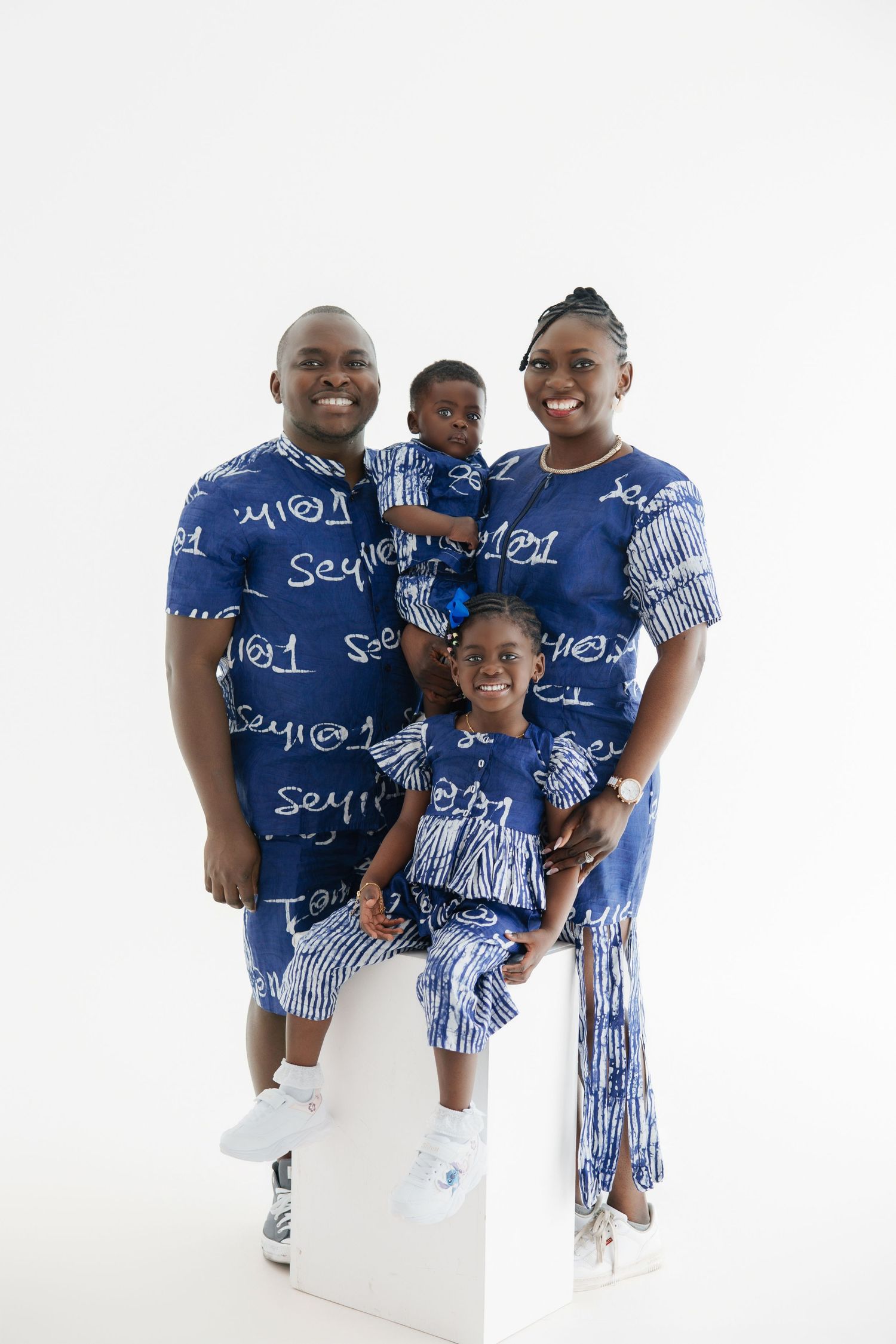 Family of four wearing matching blue printed outfits posing together for a studio portrait photo.