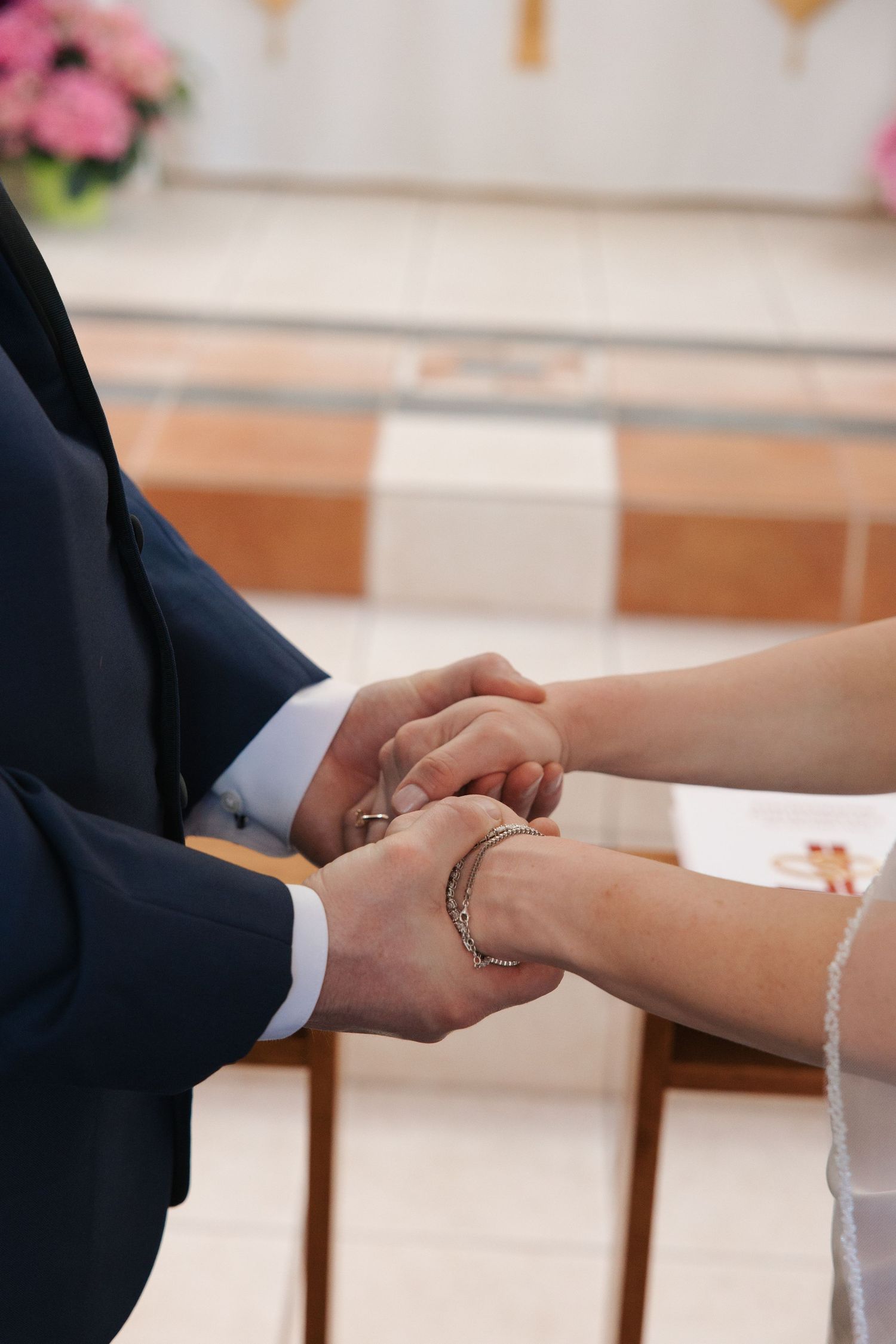 Bride and groom holding hands during wedding ceremony in church, exchanging rings at the altar.