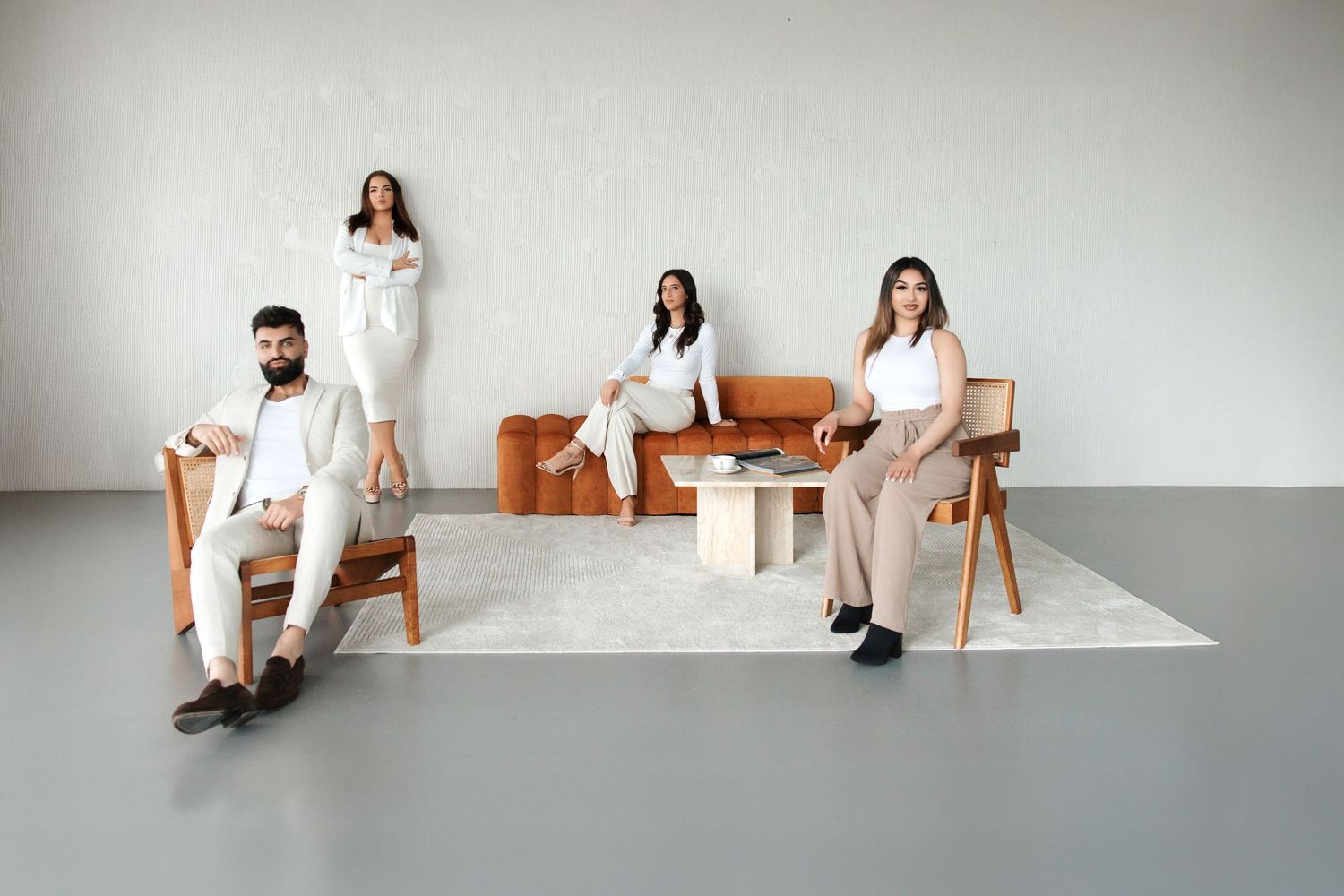 Four stylish people in neutral tones posing with modern wooden furniture against a minimalist white studio backdrop.