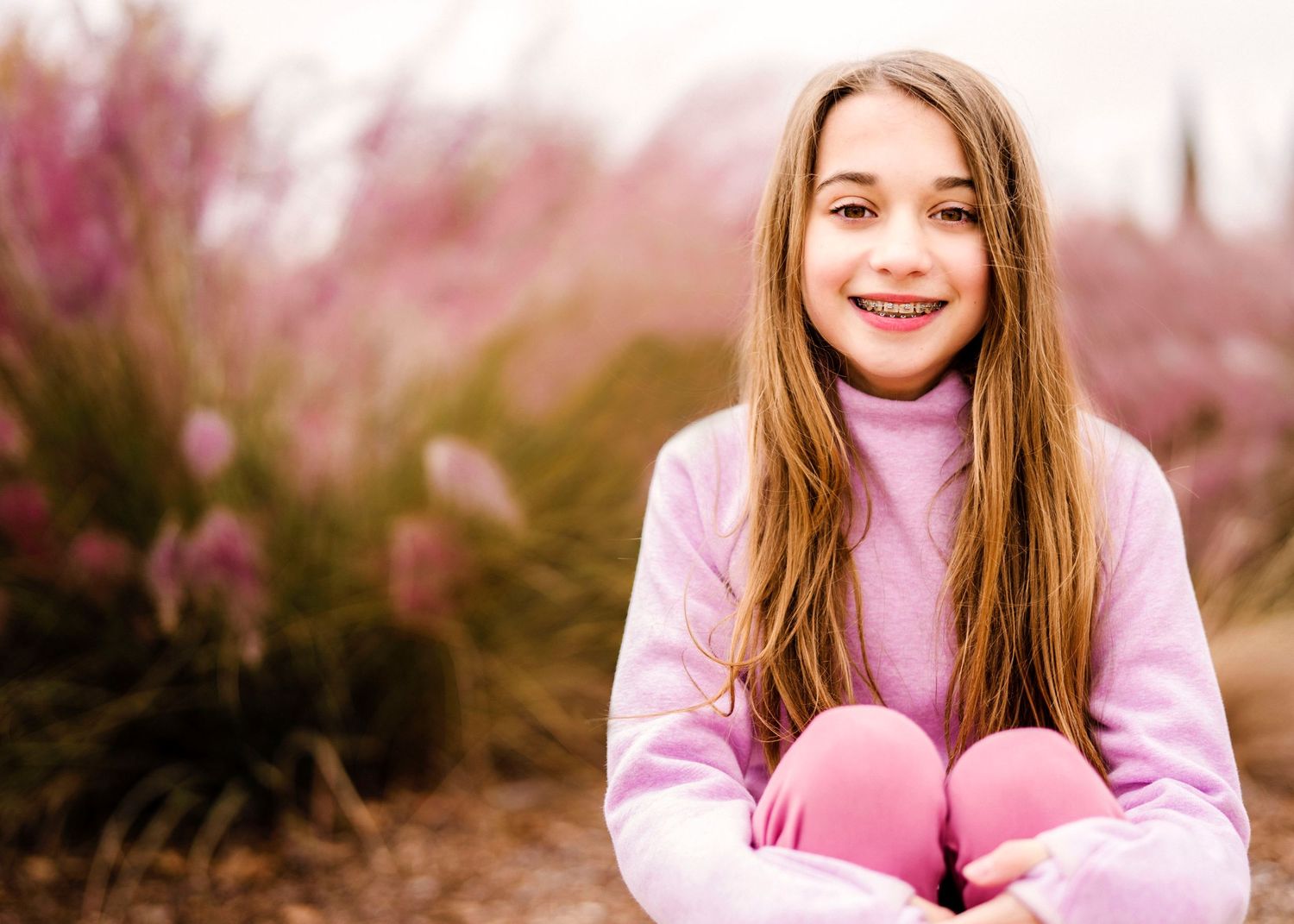 Person in pink attire sitting outdoors with cherry blossoms in the background.
