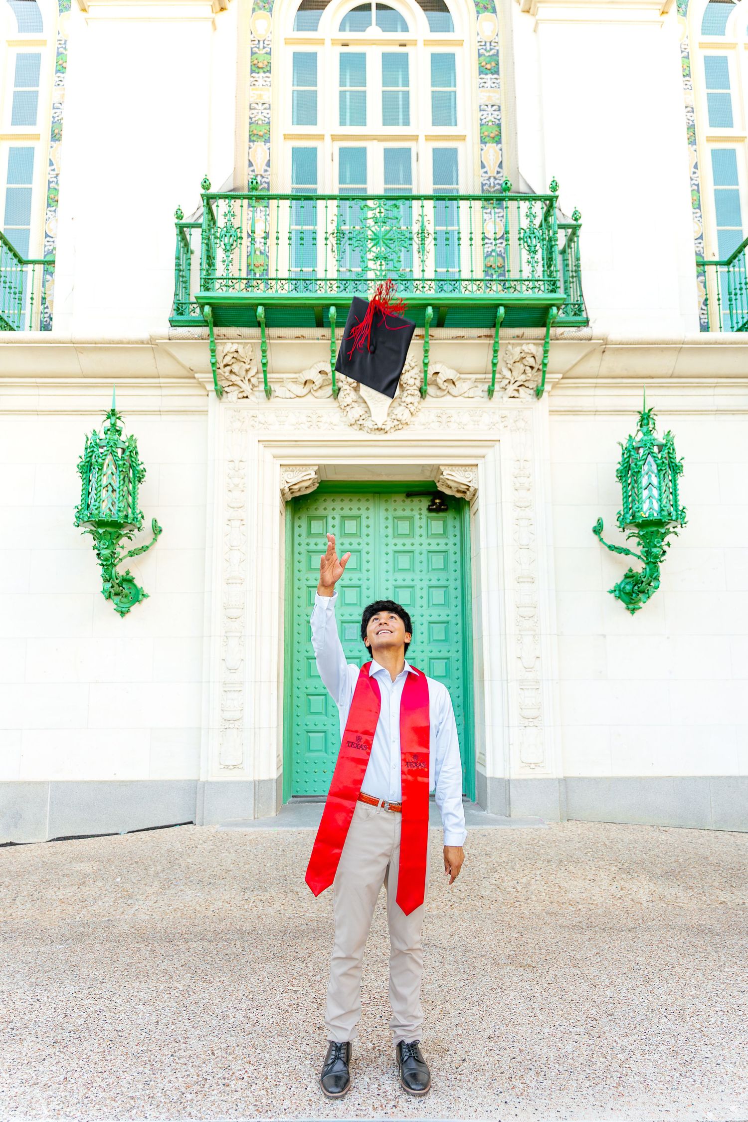 A person in a red jacket and gray pants stands in front of an ornate green and white building facade with decorative details.