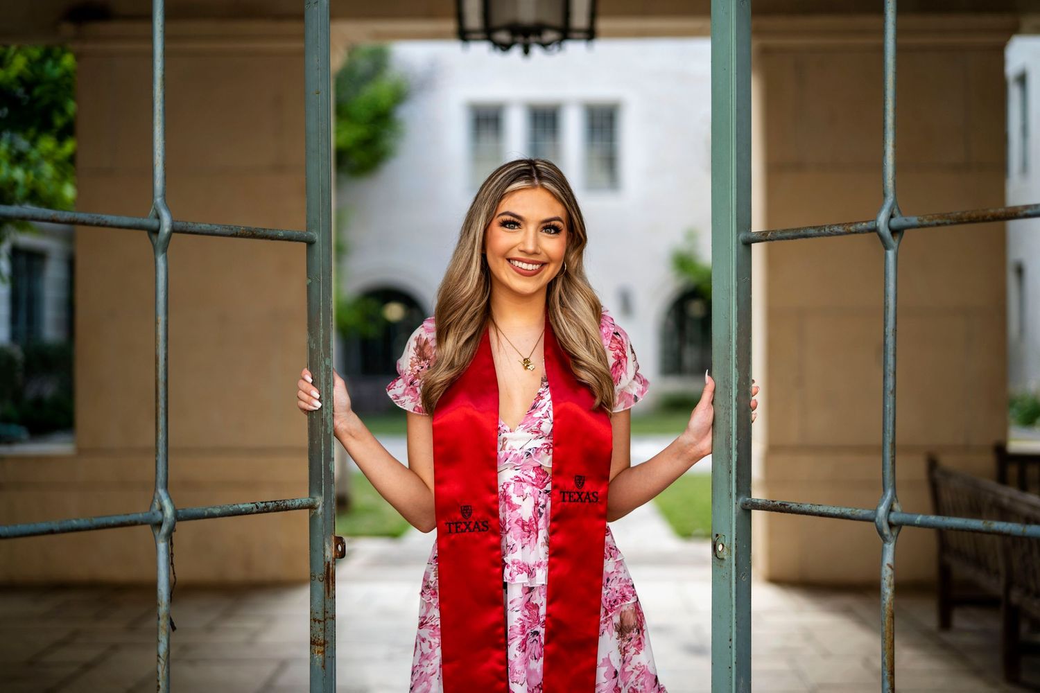 Graduate in pink floral dress and red stole stands between architectural columns.