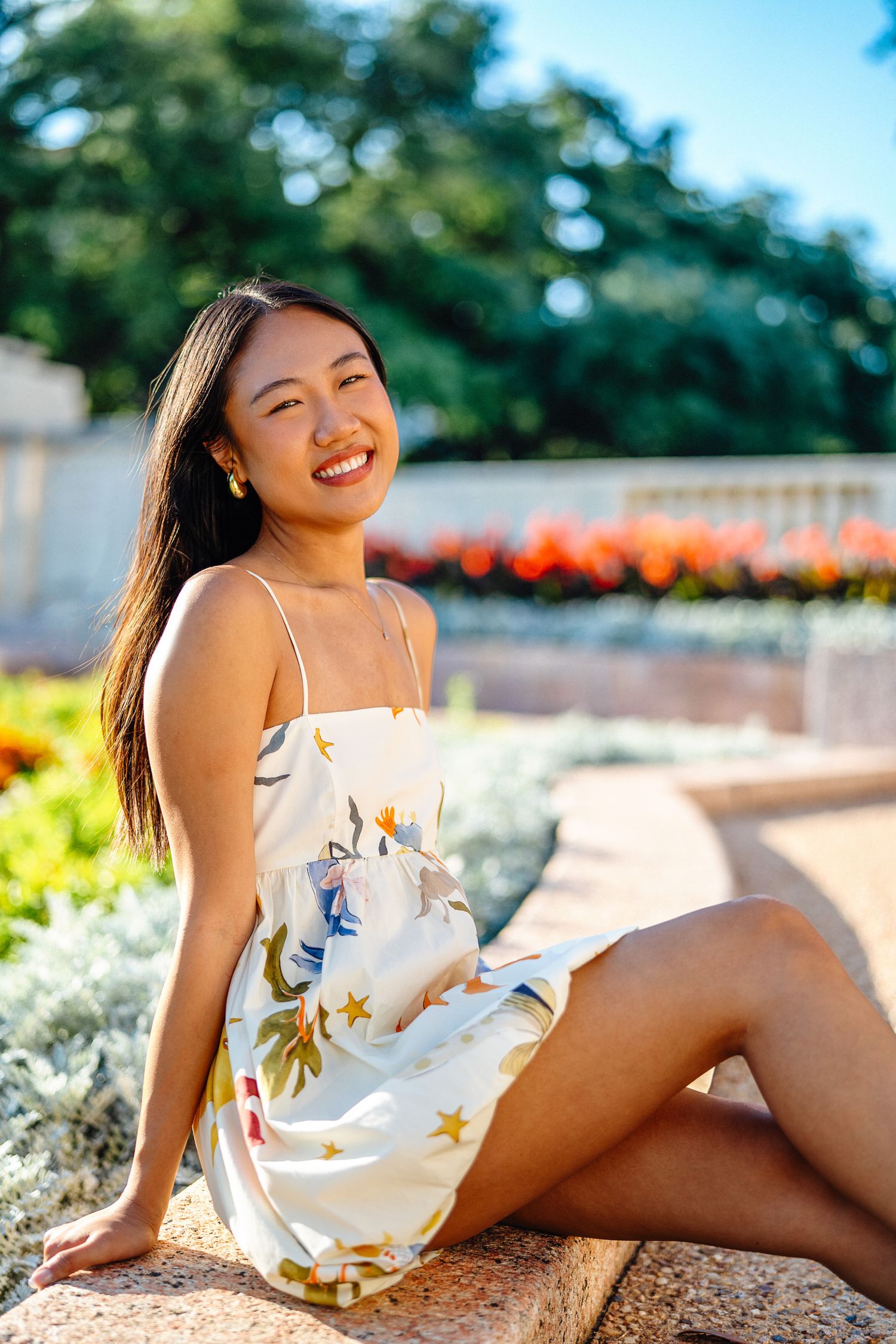 A person in a floral dress poses by garden flowers during golden hour photography session.